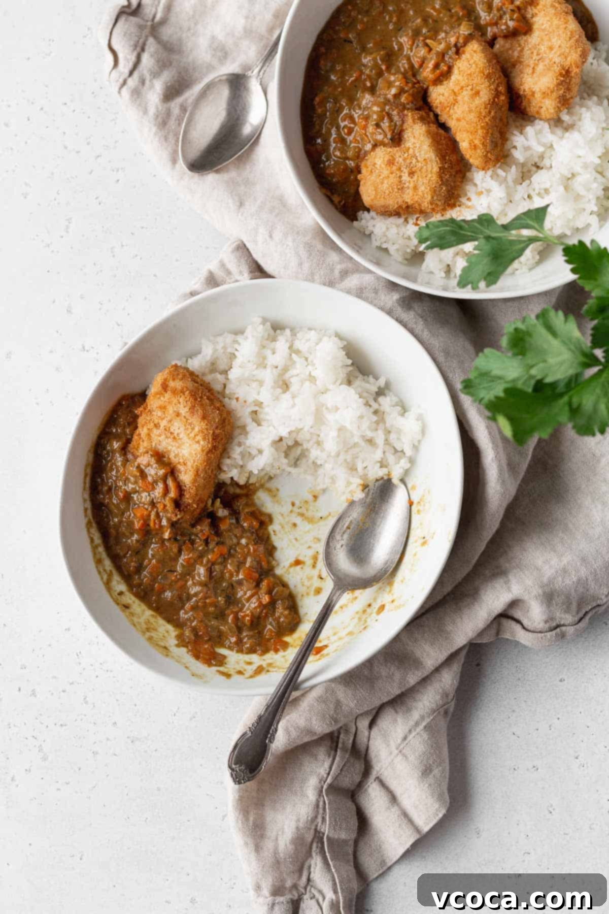 2 bowls of katsu curry on a natural linen with a silver spoon.