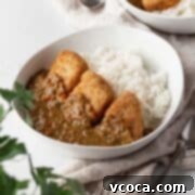 Vegan katsu curry in a white bowl on a linen with a flat leaf parsley plant in the corner of the shot.