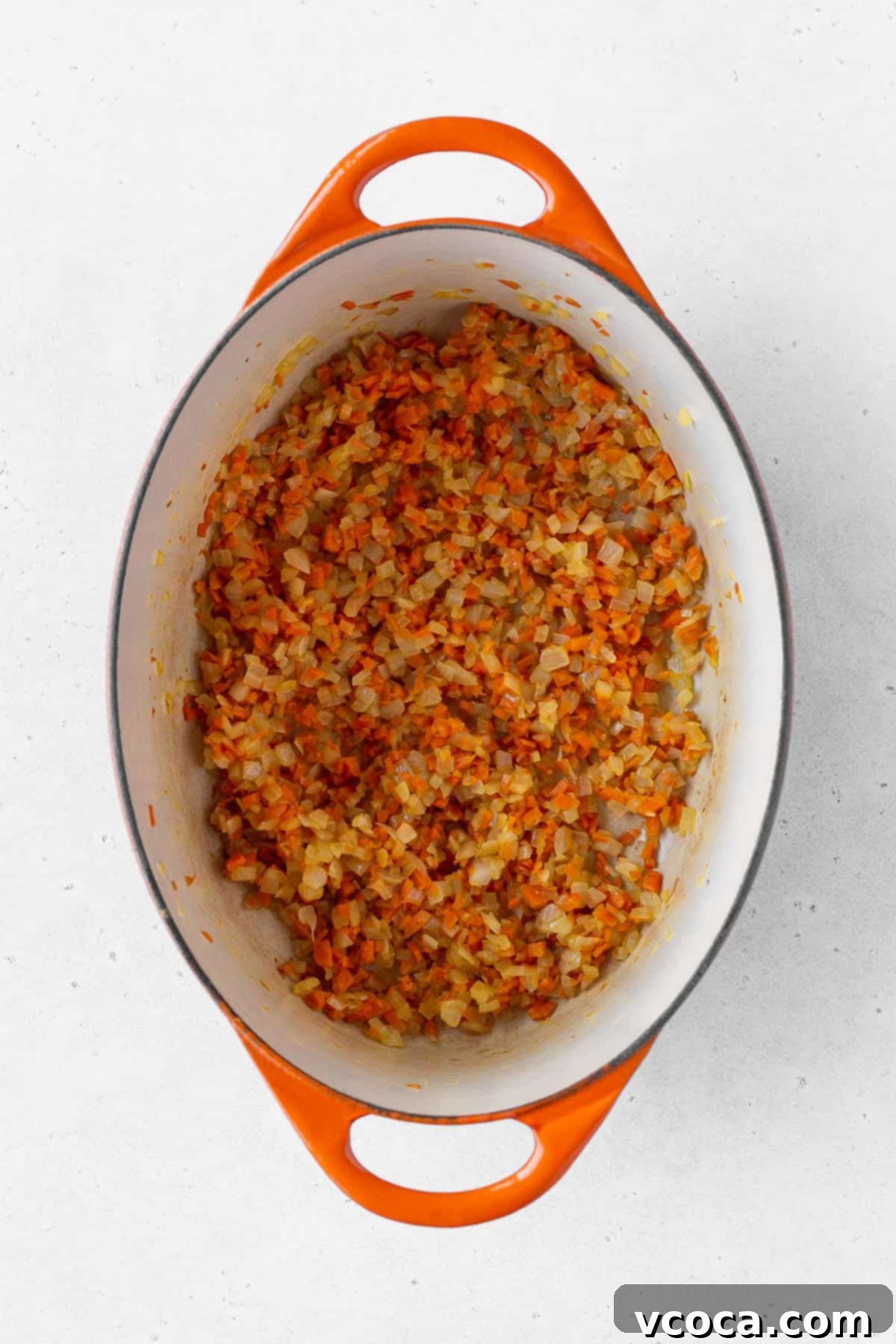 Minced onion and carrots cooking in an enameled pot.