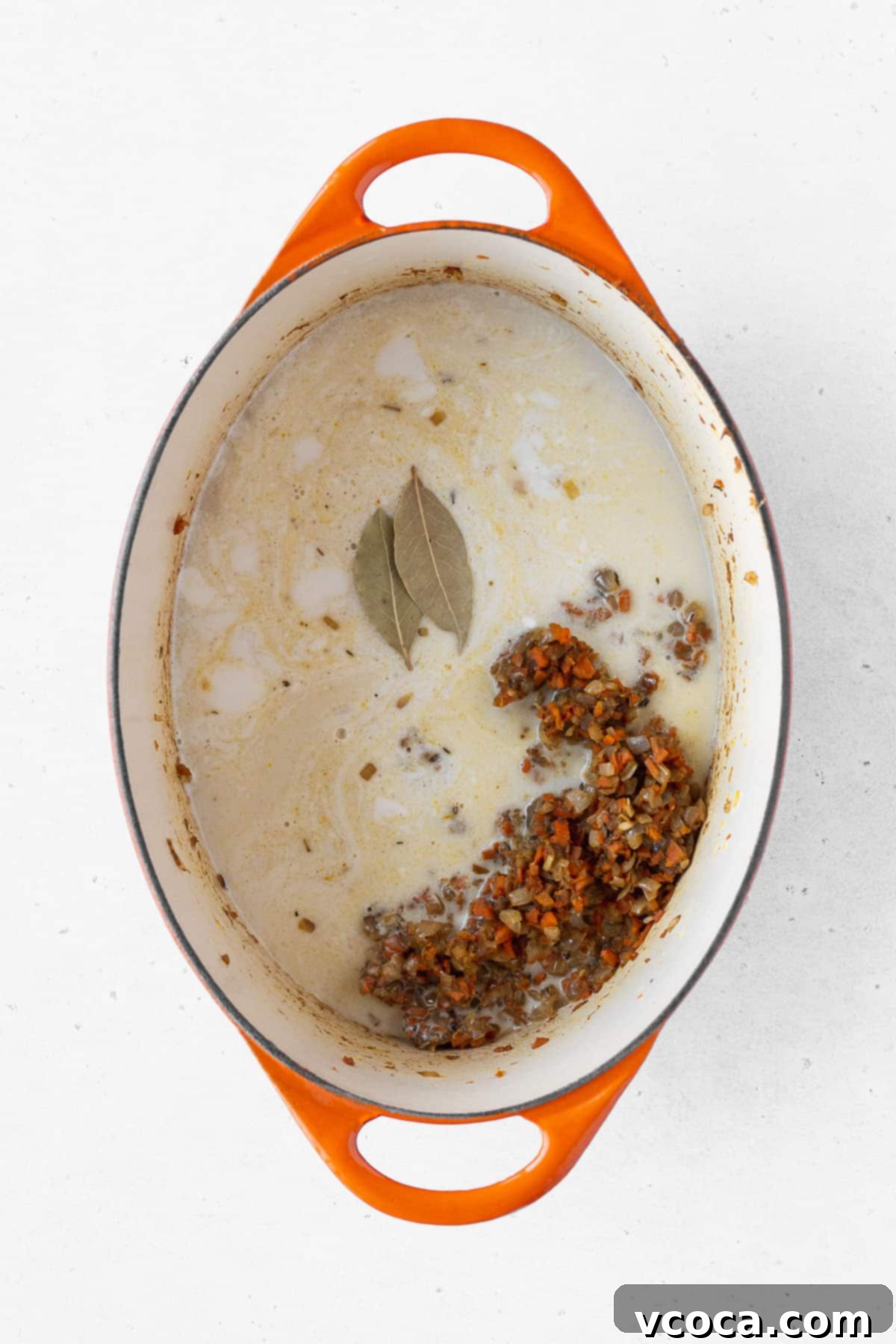Coconut milk and vegetable stock poured over the vegetables, with two bay leaves added on top.