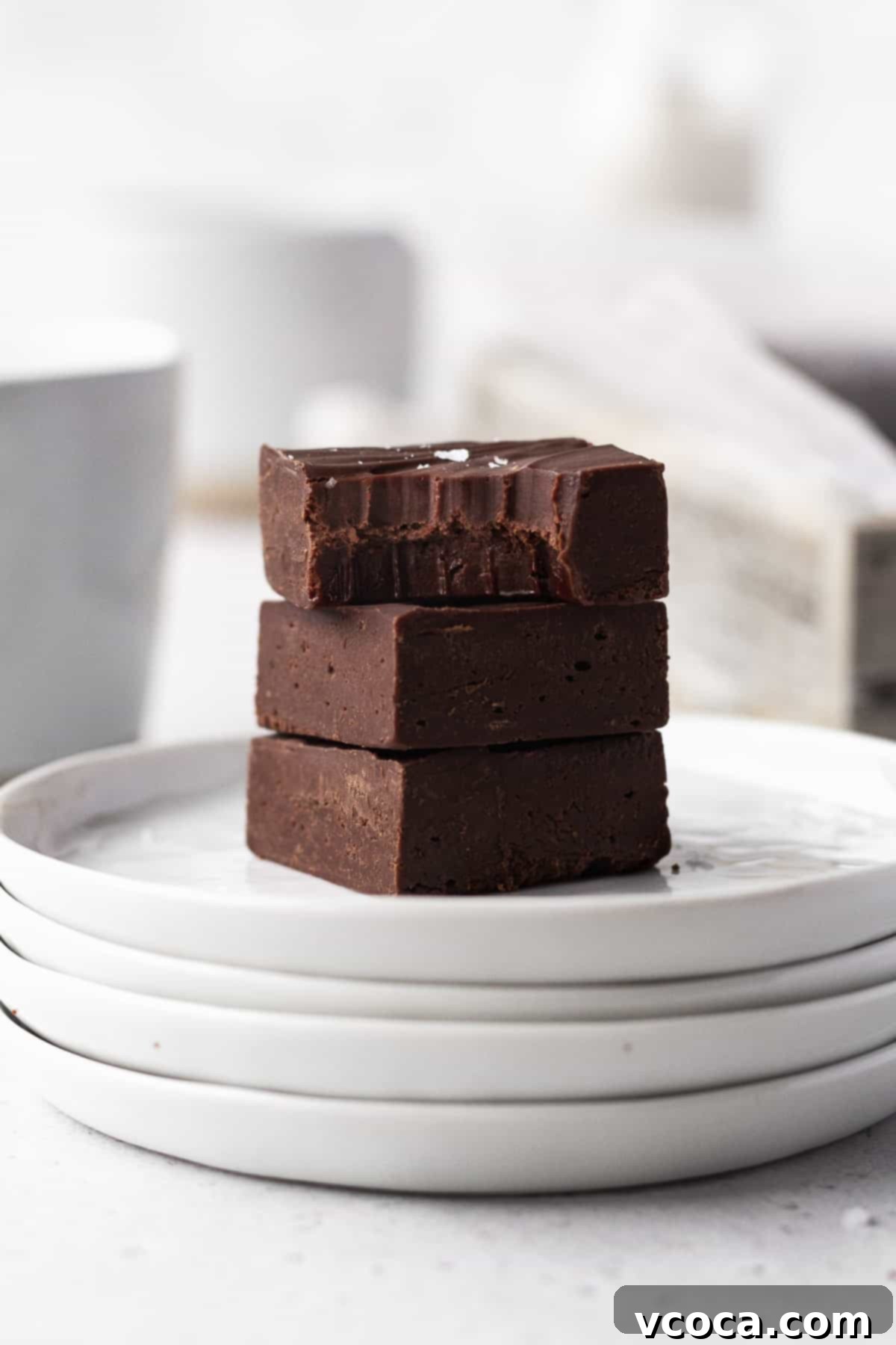 Plant-Based Fudge 10 Side on shot of 3 cubes of dairy-free fudge stacked on a stack of white plates with the top square having a bite taken out.