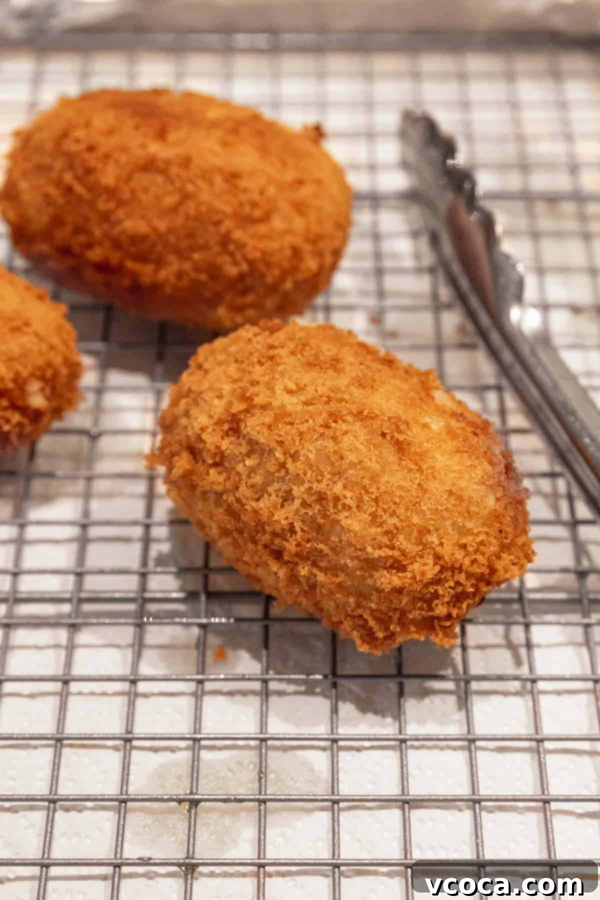 Plant-Powered Potato Croquettes 16 Close up shot of a golden, crispy potato croquette draining on a wire rack above paper towels.