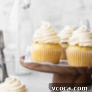 Square hero shot of a dairy free vanilla cupcakes on a wooden cake stand.
