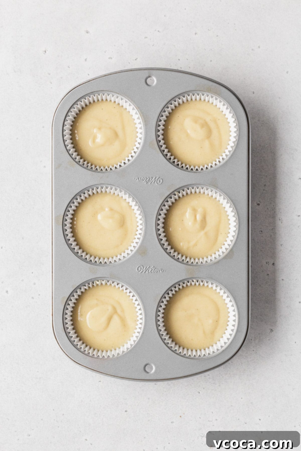 Muffin tin filled with white paper liners and dairy-free vanilla cupcake batter before baking.