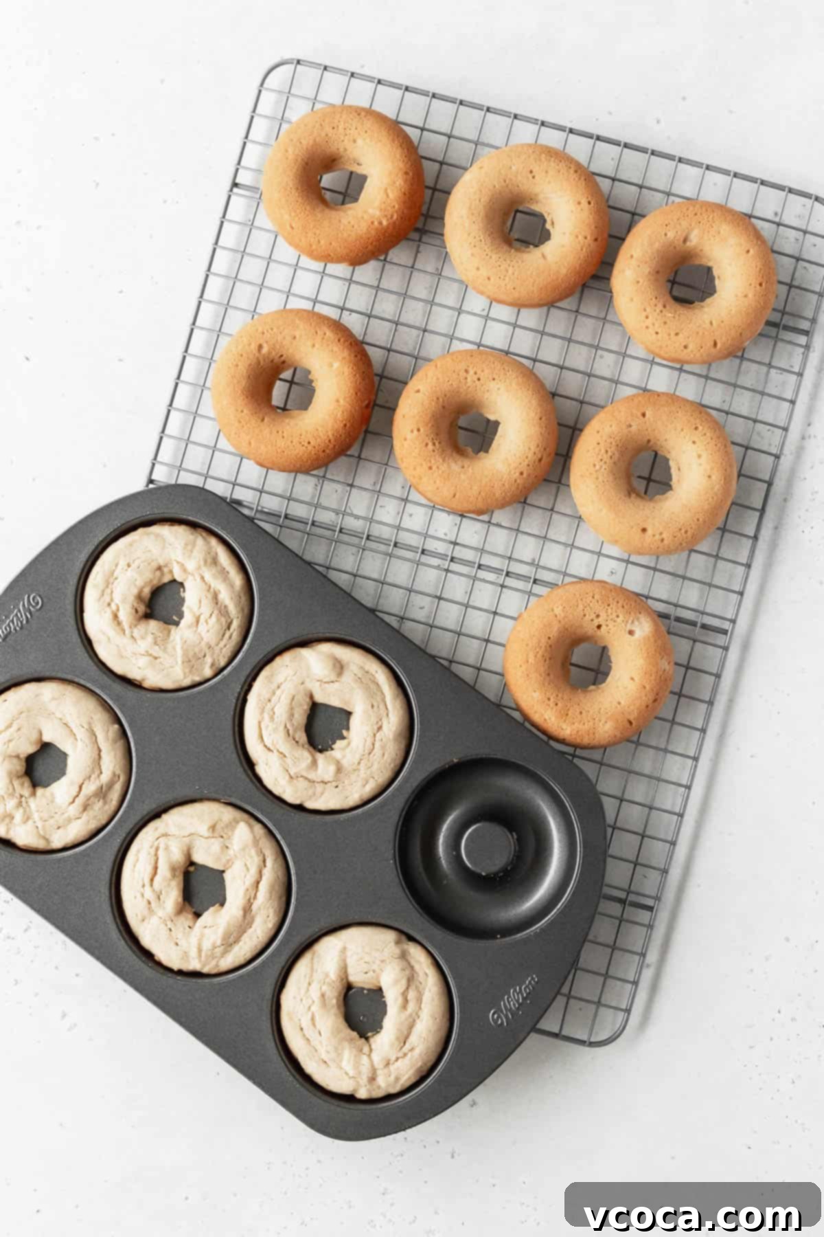 Wholesome Plant-Based Baked Donuts 9 Overhead shot of a pan of gluten free dairy free doughnuts on a wire rack with more donuts that have been removed the pan are cooling.