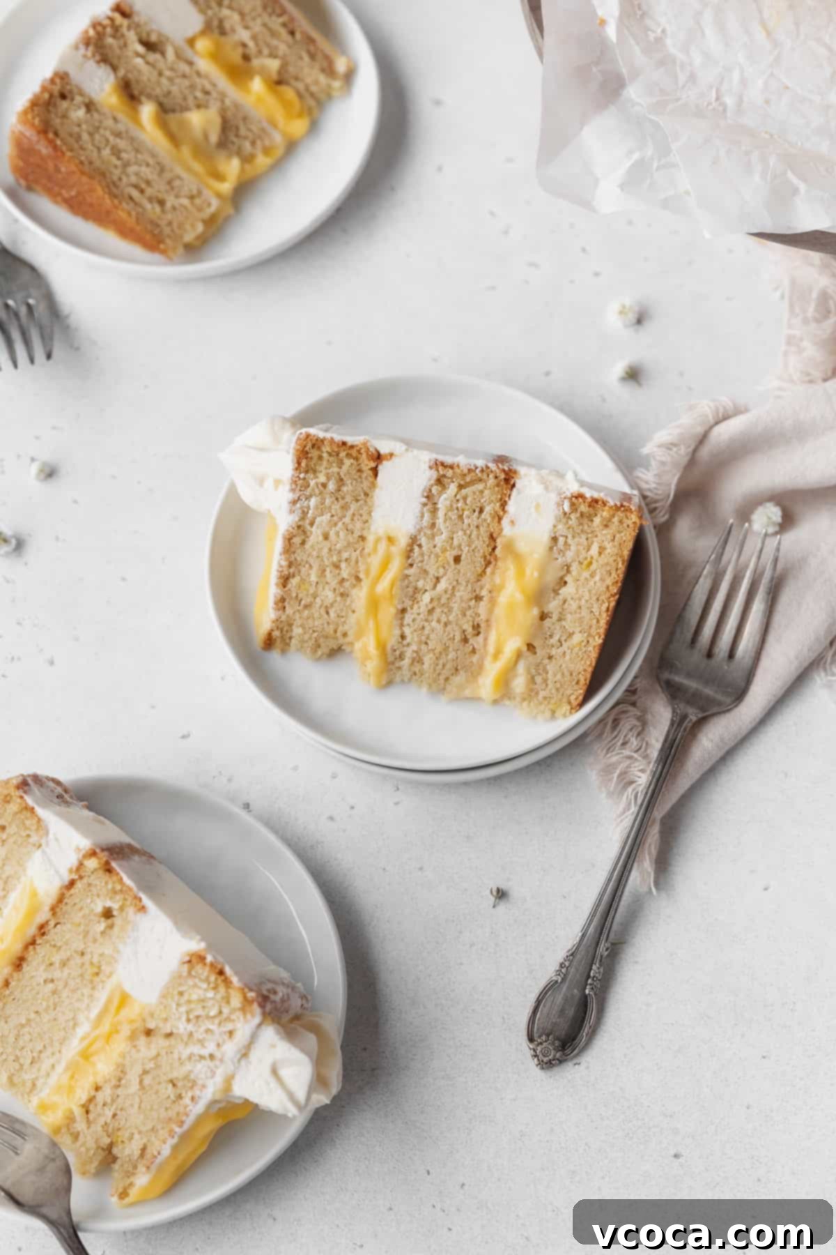 Luscious Lemon Curd Cake 28 Overhead shot of 3 slices of dairy-free lemon curd layer cake on white dessert plates with silver forks.