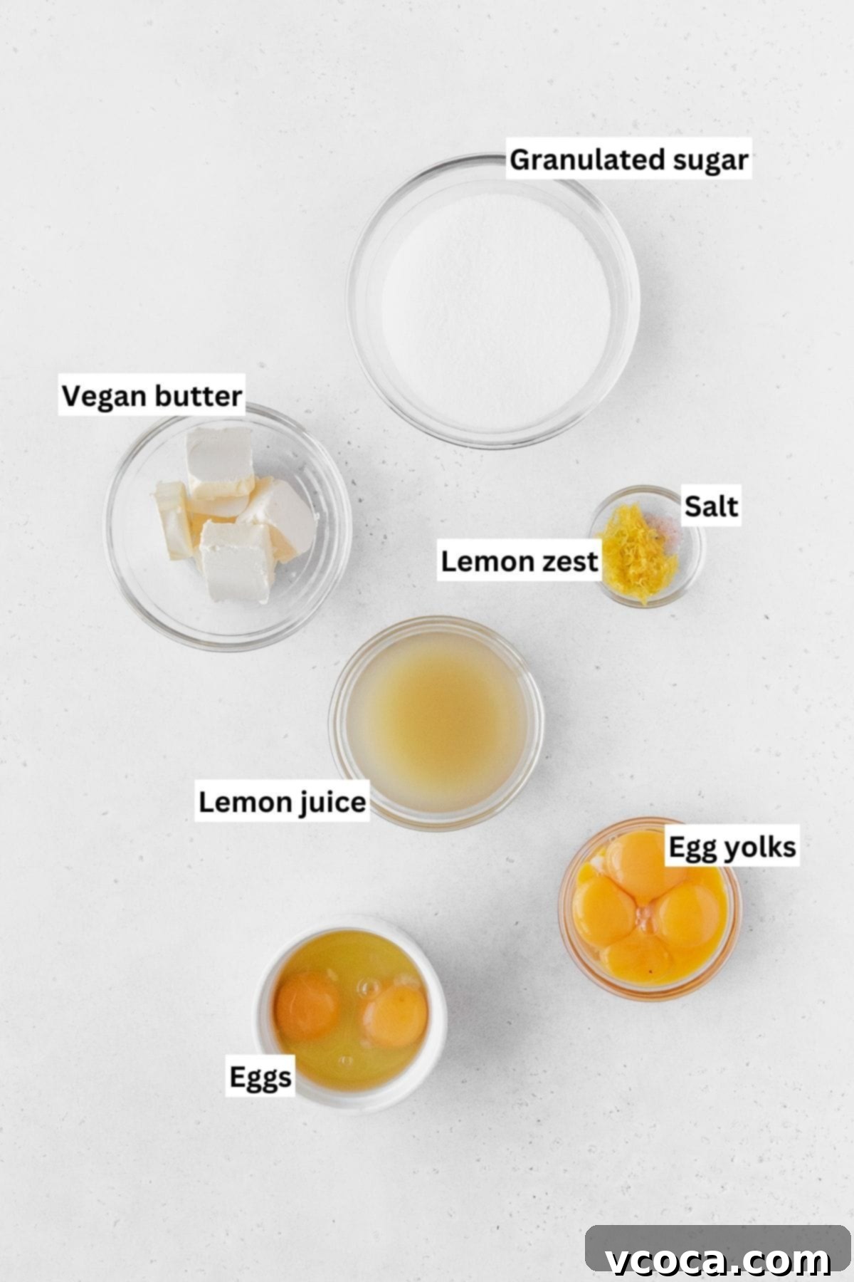 Luscious Lemon Curd Cake 6 Lemon curd ingredients measured out into small glass bowls on a white table with text overlay.