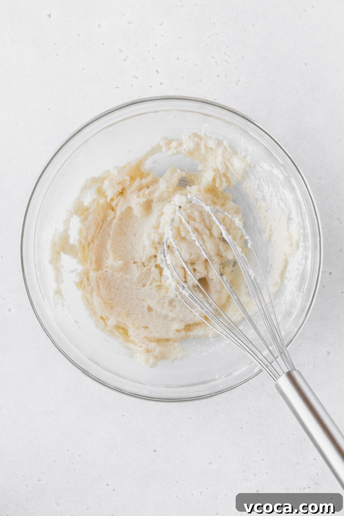 Luscious Lemon Curd Cake 7 Mixing together the sugar, salt, lemon zest, and eggs in a glass bowl with a silver whisk.