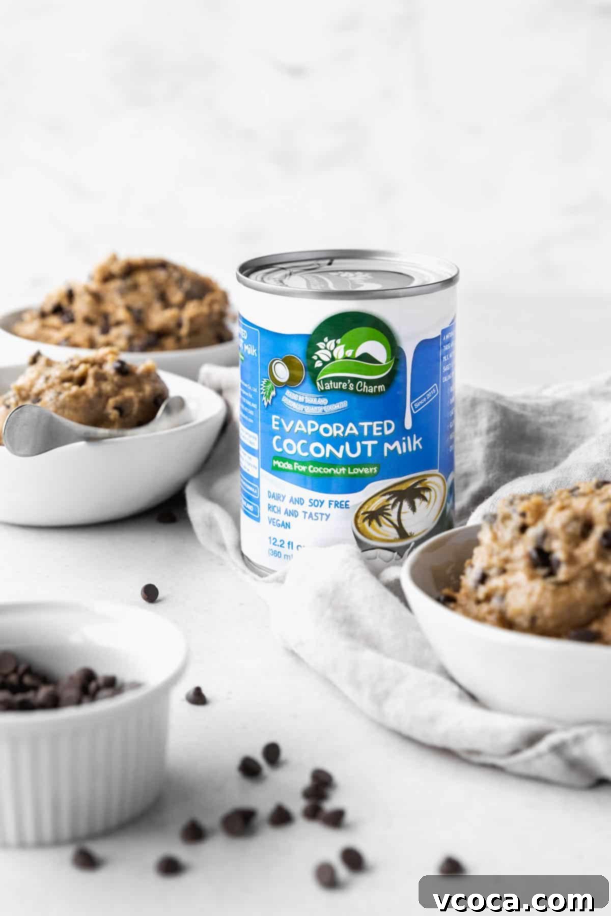 No-Bake Gluten-Free Cookie Dough 4 Can of Nature's Charm evaporated coconut milk in the center of an array of bowls filled with vegan edible cookie dough.
