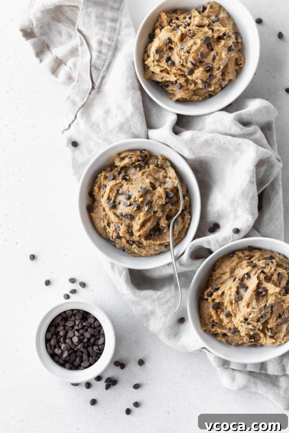 No-Bake Gluten-Free Cookie Dough 10 Overhead hero shot of 3 bowls of gluten-free cookie dough with silver spoon in the middle bowl and a small bowl of mini chocolate chips to the side.
