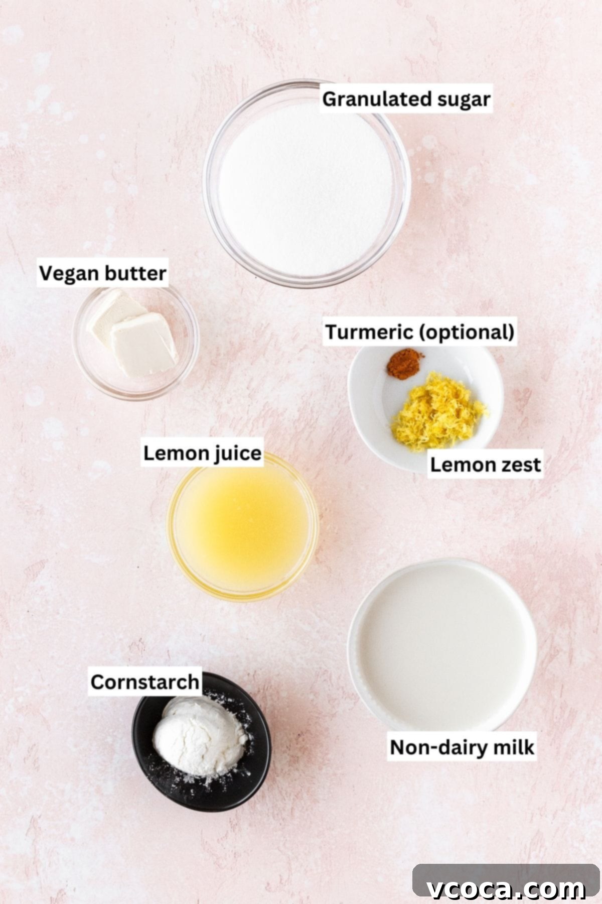 Ingredients needed for making vegan lemon curd measured out into bowls on a pink table with text overlay, including lemons, vegan butter, sugar, cornstarch, and plant milk.
