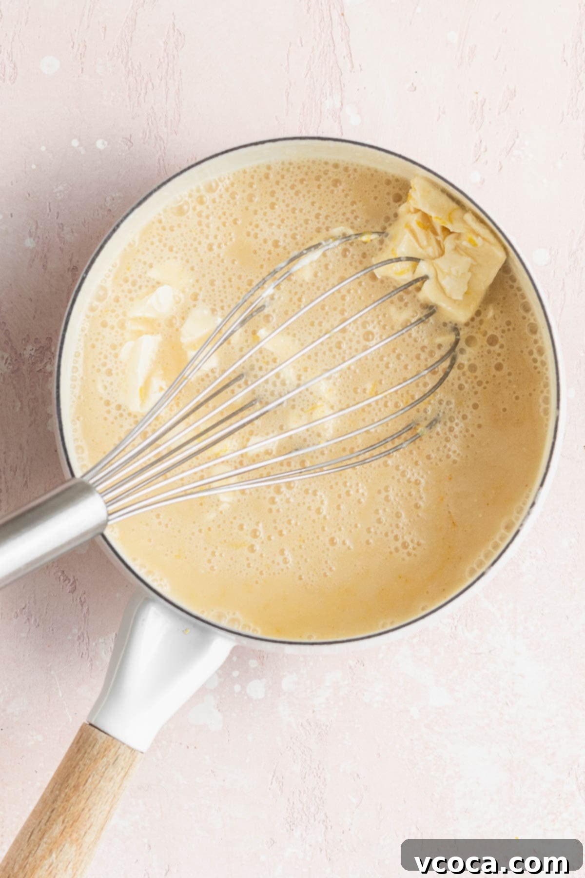 Whisking the butter into the warmed vegan lemon curd mixture in a saucepan to combine ingredients thoroughly.