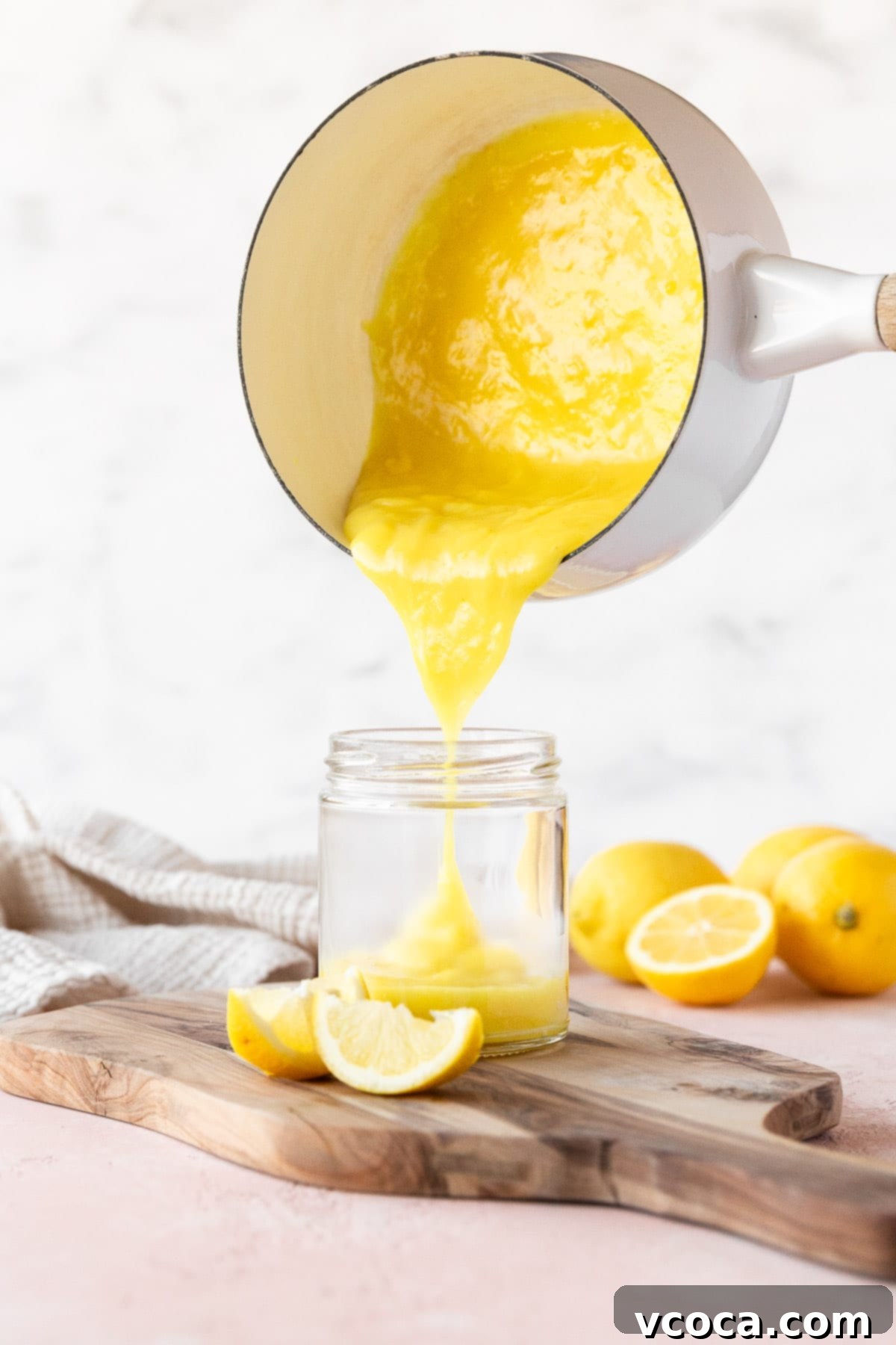 Pouring the vegan lemon curd from a saucepan into a mason jar, capturing its smooth and vibrant consistency.