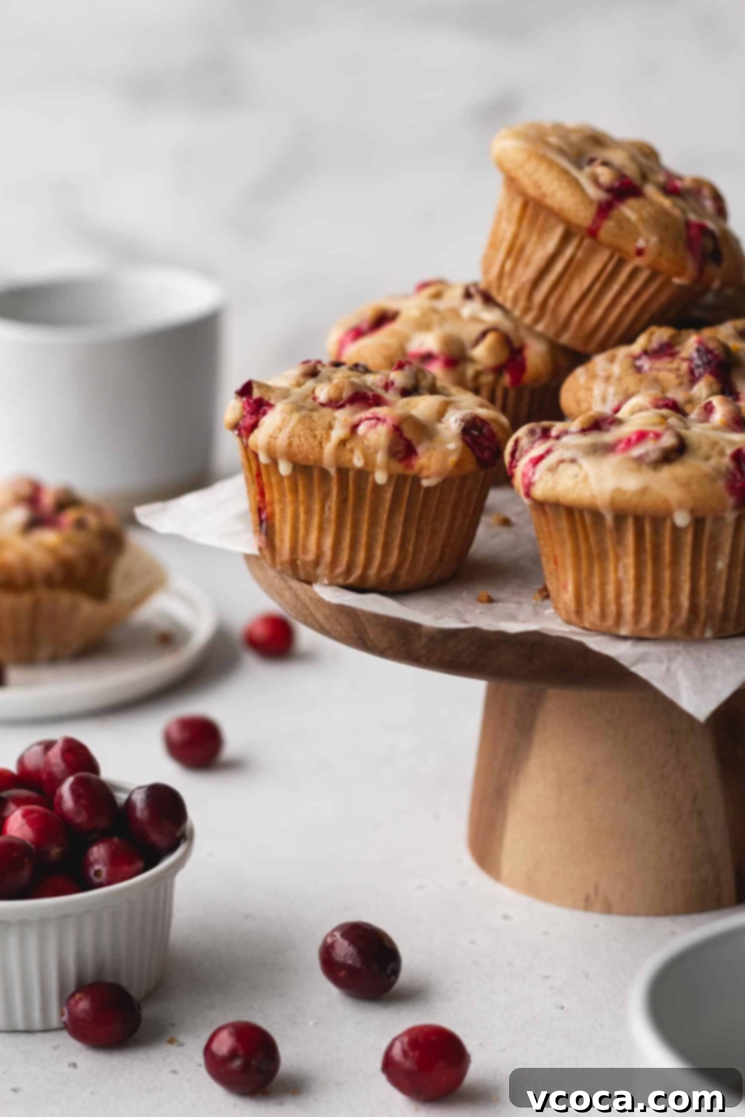 Zesty Orange Cranberry Muffins 4 A beautiful display of golden-domed gluten-free cranberry orange muffins artfully arranged on an elegant white cake stand, highlighting their inviting aroma and delicious appeal for any gathering.