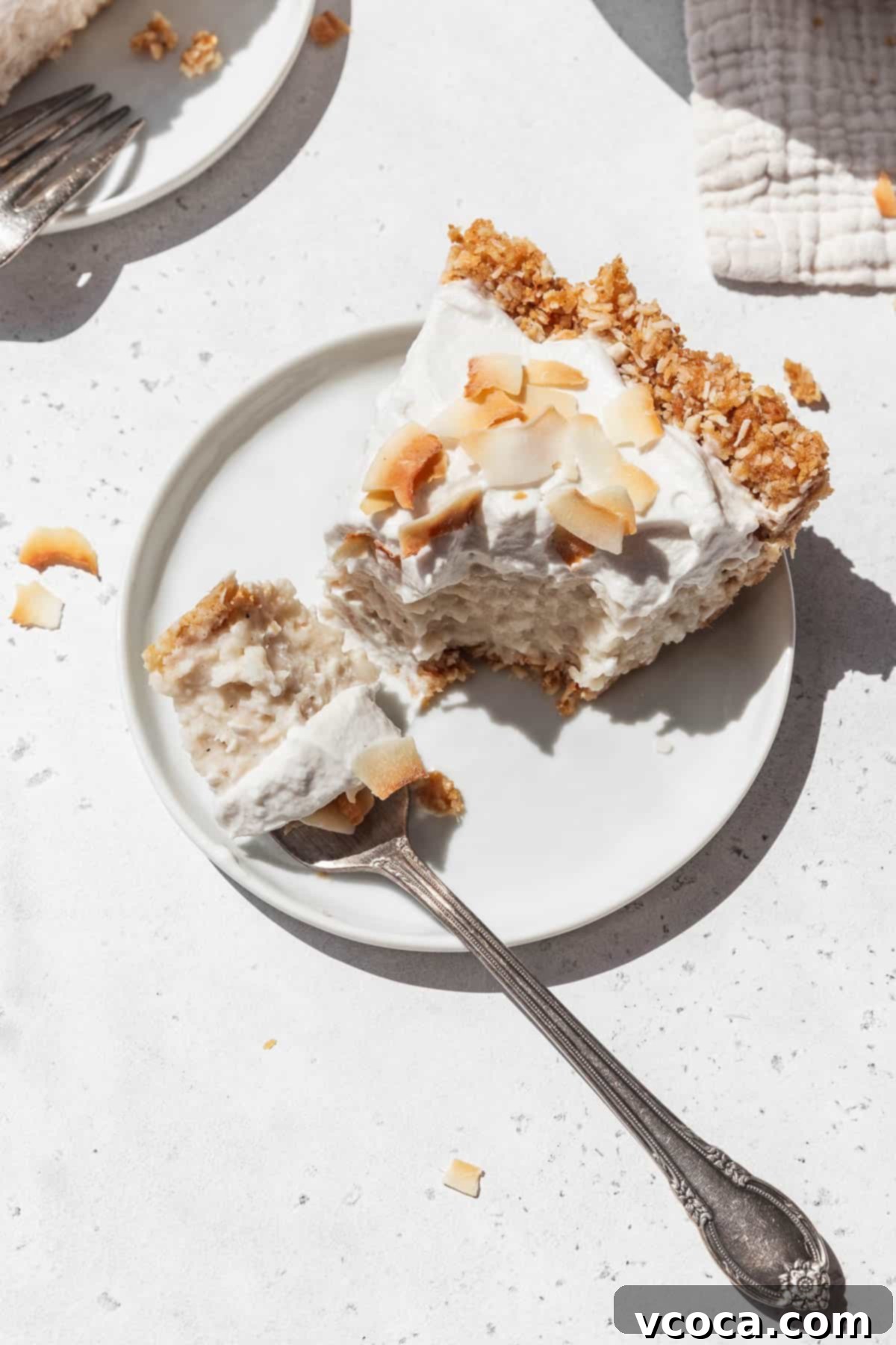 Divine Vegan Coconut Cream Pie Gluten Free 16 Small white dessert plate with a slice of GF no-bake plant-based coconut cream pie with a silver fork taking a bite out of it.