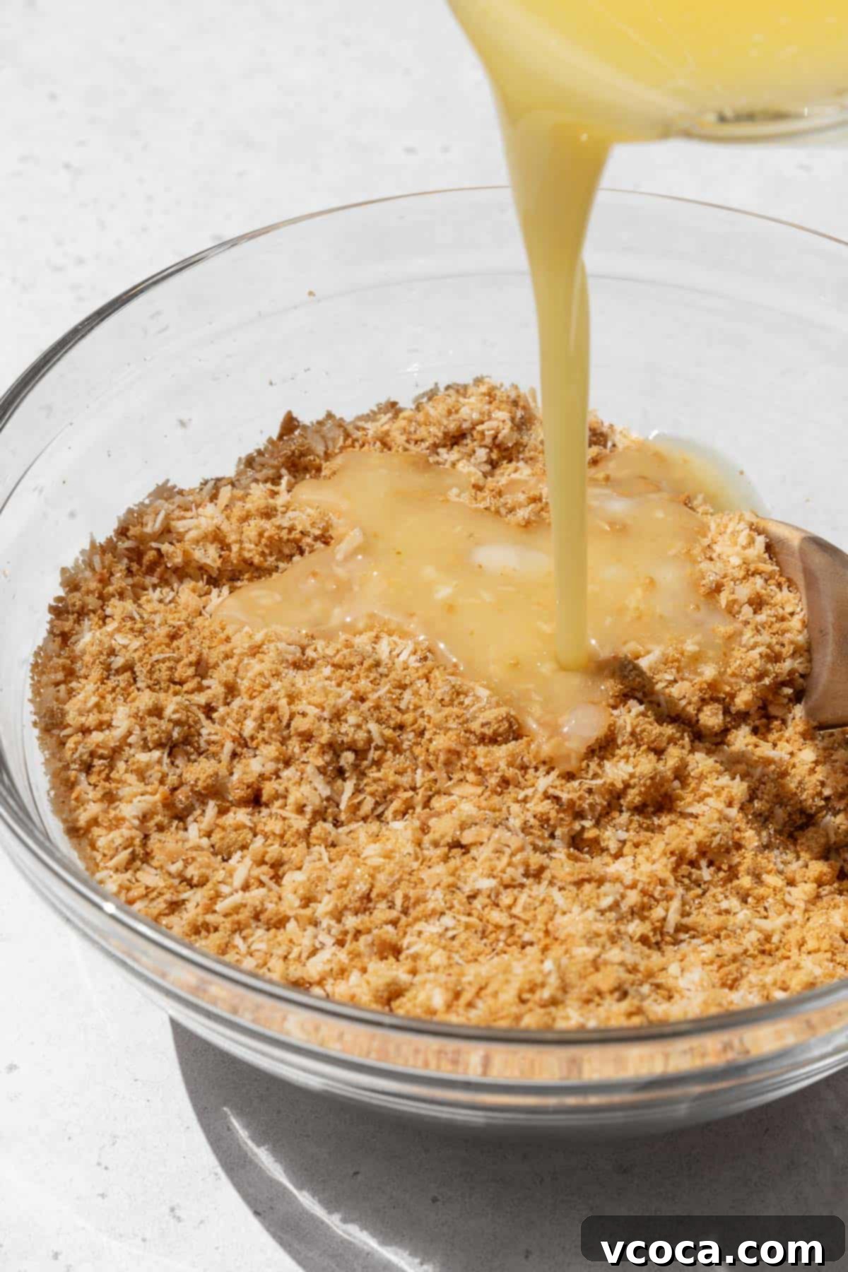 Divine Vegan Coconut Cream Pie Gluten Free 5 Action shot of melted vegan butter being poured into the bowl with the graham cracker crumb and toasted coconut mixture.