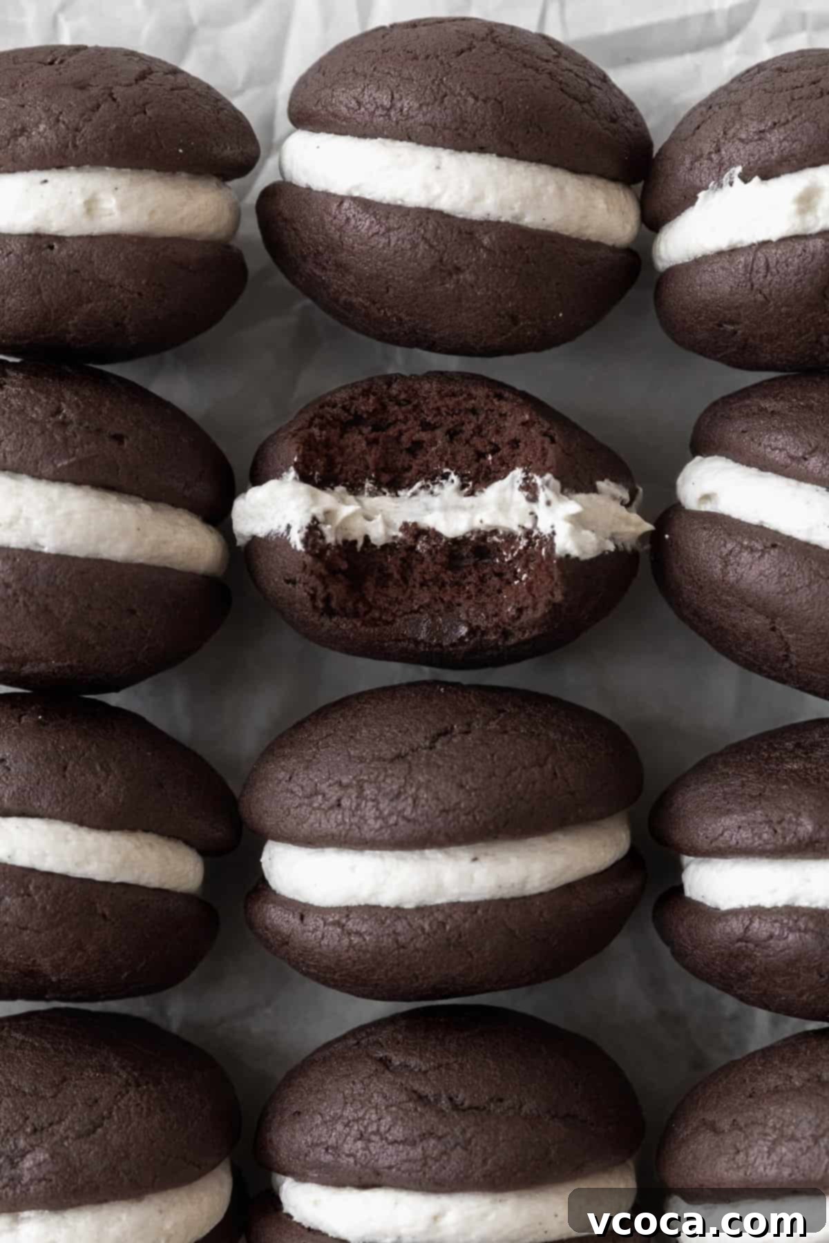 Gluten-Free Whoopie Pies 2 Gluten-free whoopie pies on a white sheet of parchment paper. One of the cookies has a bite taken out of it.
