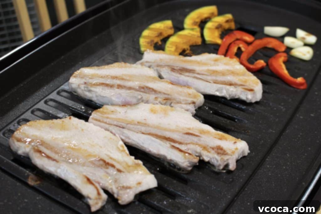 Pork belly and vegetables sizzling on a tabletop grill for Whole30 Samgyeopsal.