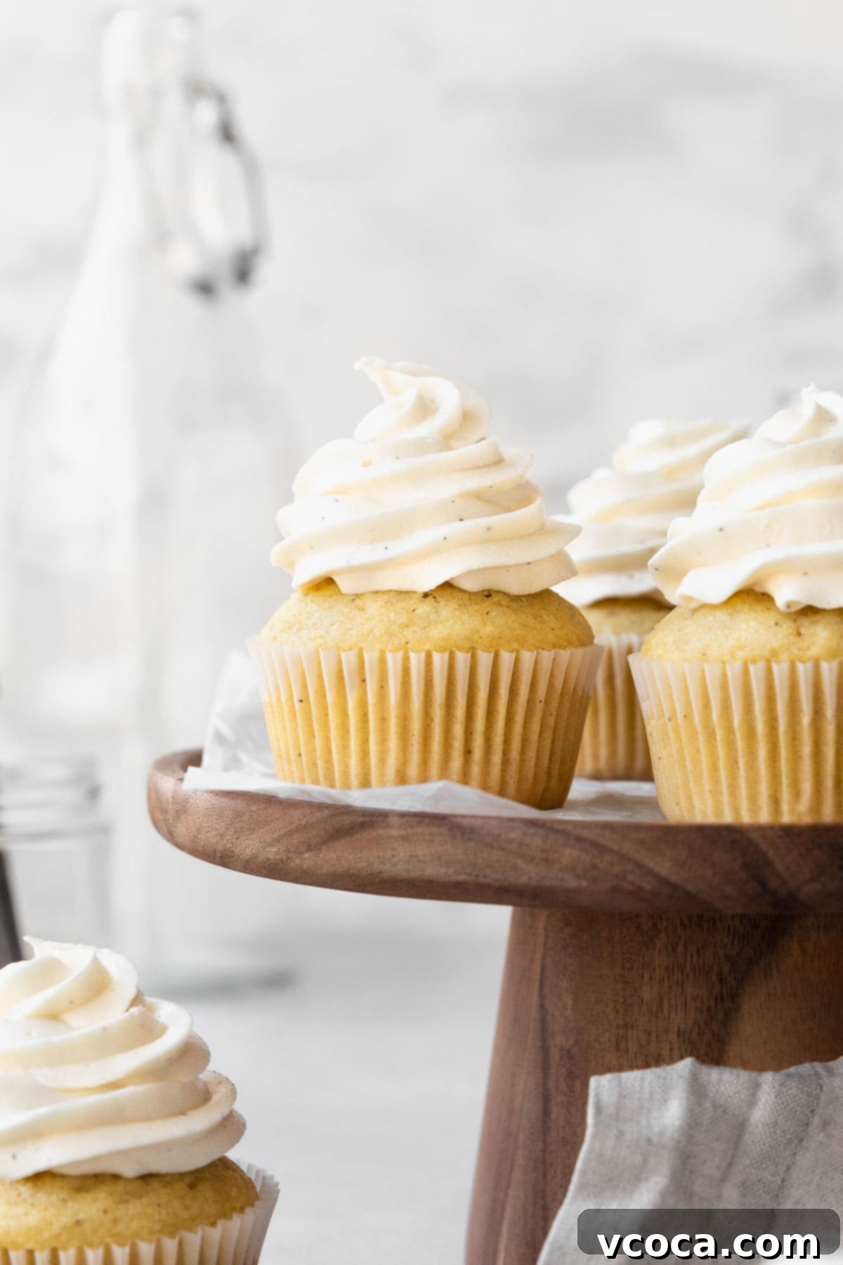 Velvety Vegan Buttercream 2 Side on shot of vanilla buttercream topped vegan cupcakes on a wooden cake platter.