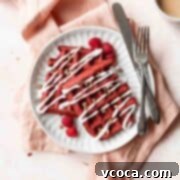 A square shot of a white plate of red velvet waffles with cream cheese drizzle and pecans.