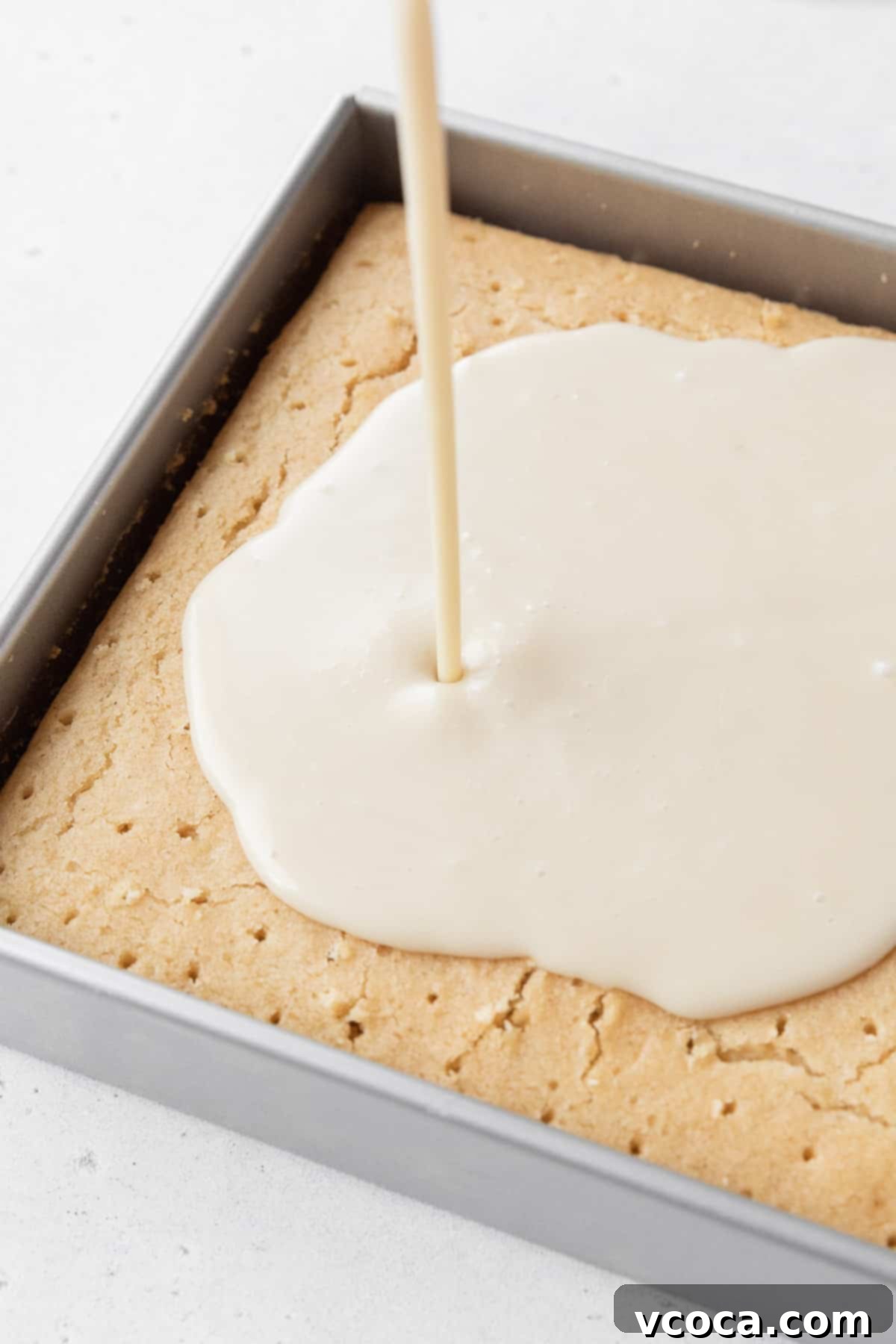 The rich dairy-free tres leches milk soak being generously poured over the cake, which has been meticulously pricked with holes to ensure maximum absorption and a wonderfully moist texture.