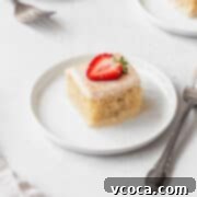 A square shot of a delicious slice of gluten-free tres leches cake, artfully placed on a white dessert plate and adorned with a fresh slice of strawberry, indicating its allergen-friendly and delectable nature.