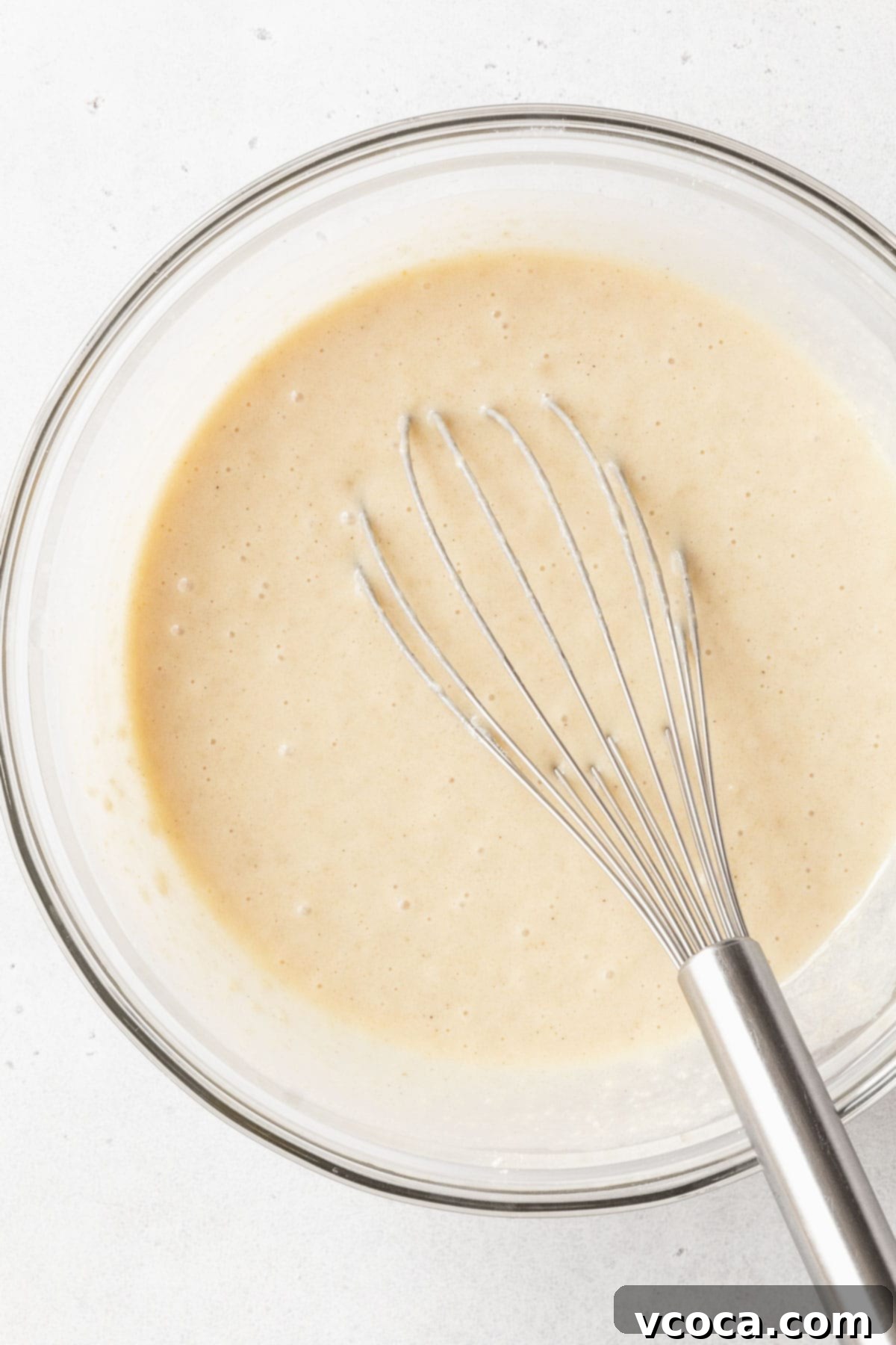 The impeccably whisked wet ingredients in a clear glass mixing bowl, forming a smooth and uniform mixture, perfectly ready to be combined with the dry components for the gluten-free and dairy-free tres leches cake.