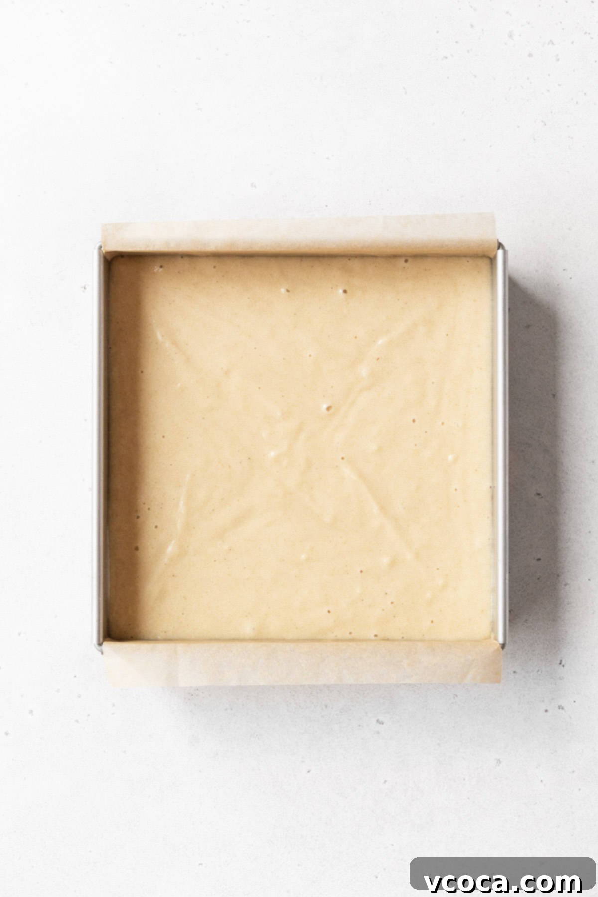 An 8x8-inch baking pan holds the unbaked gluten-free and dairy-free tres leches cake batter, its surface smooth and ready for the oven, promising a delicious dessert to come.