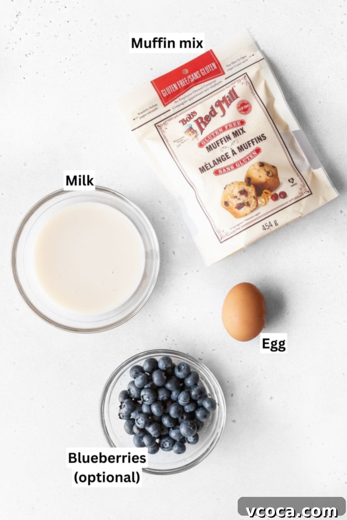 Ingredients needed to make muffin mix pancake measured out into bowls on a white table.