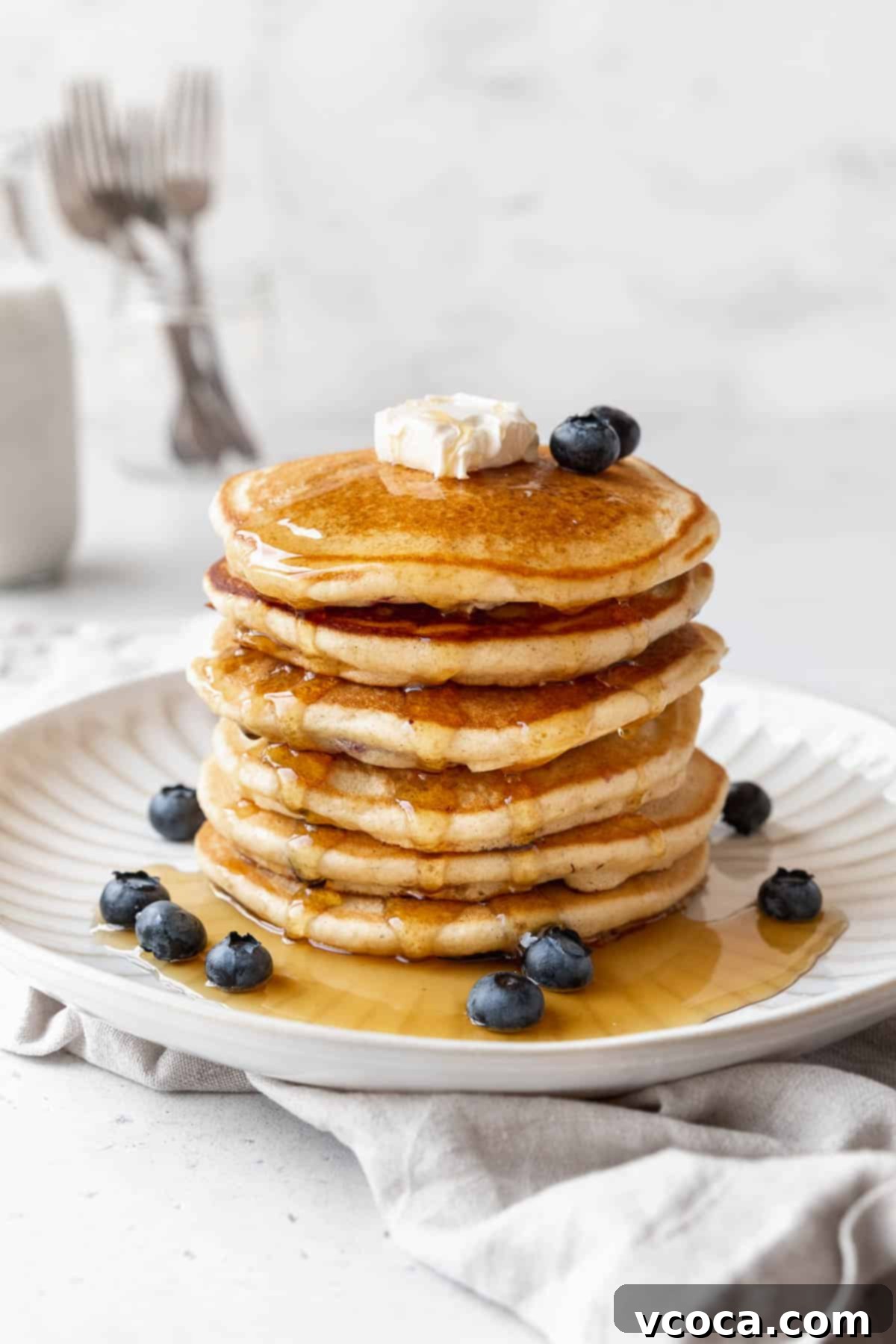 45 degree angle shot of a stack of muffin mix pancakes with blueberries, syrup, and butter.