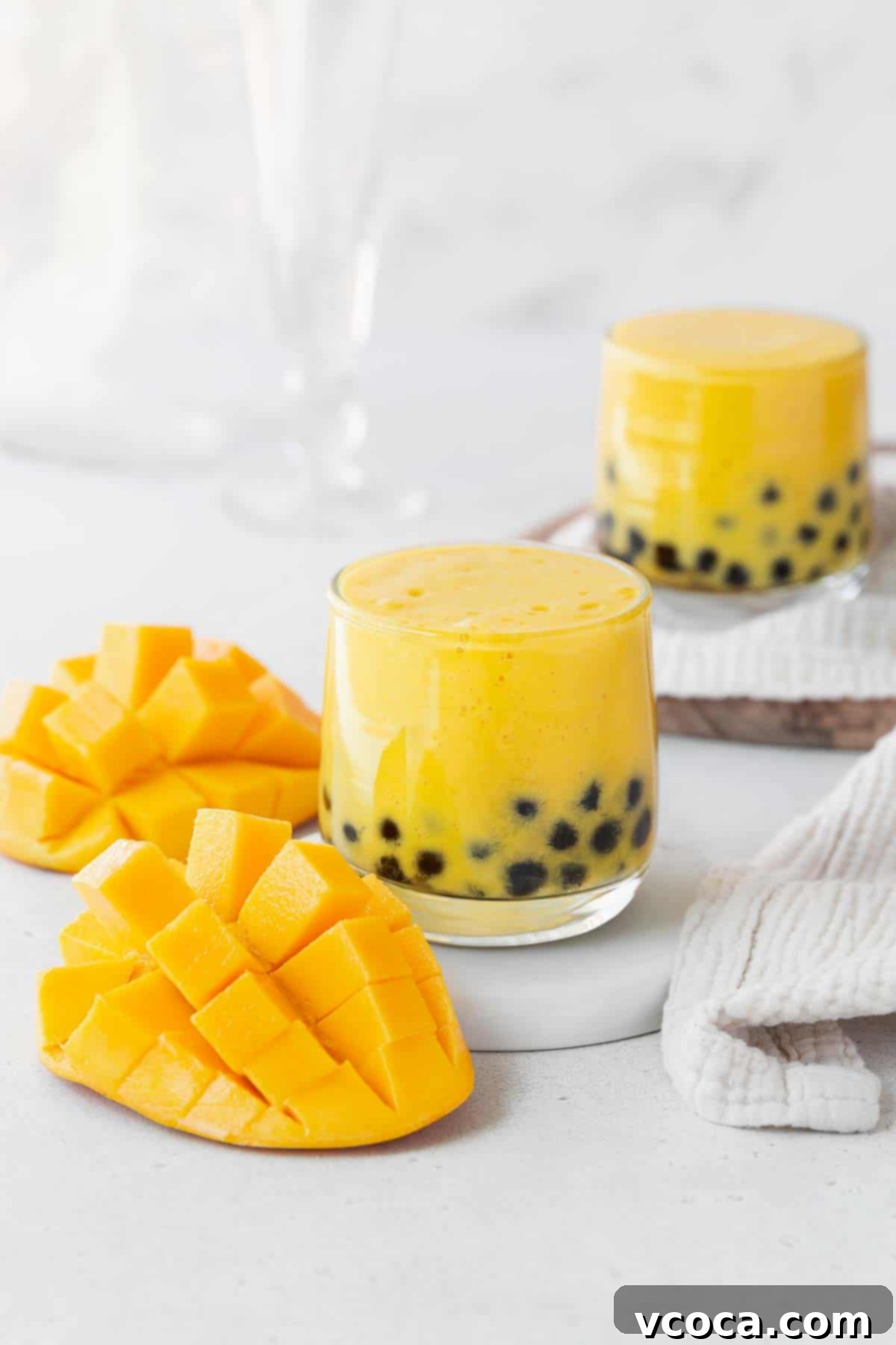 Tropical Mango Boba 2 Two glasses of mango boba tea on a white counter next to a cubed up mango.
