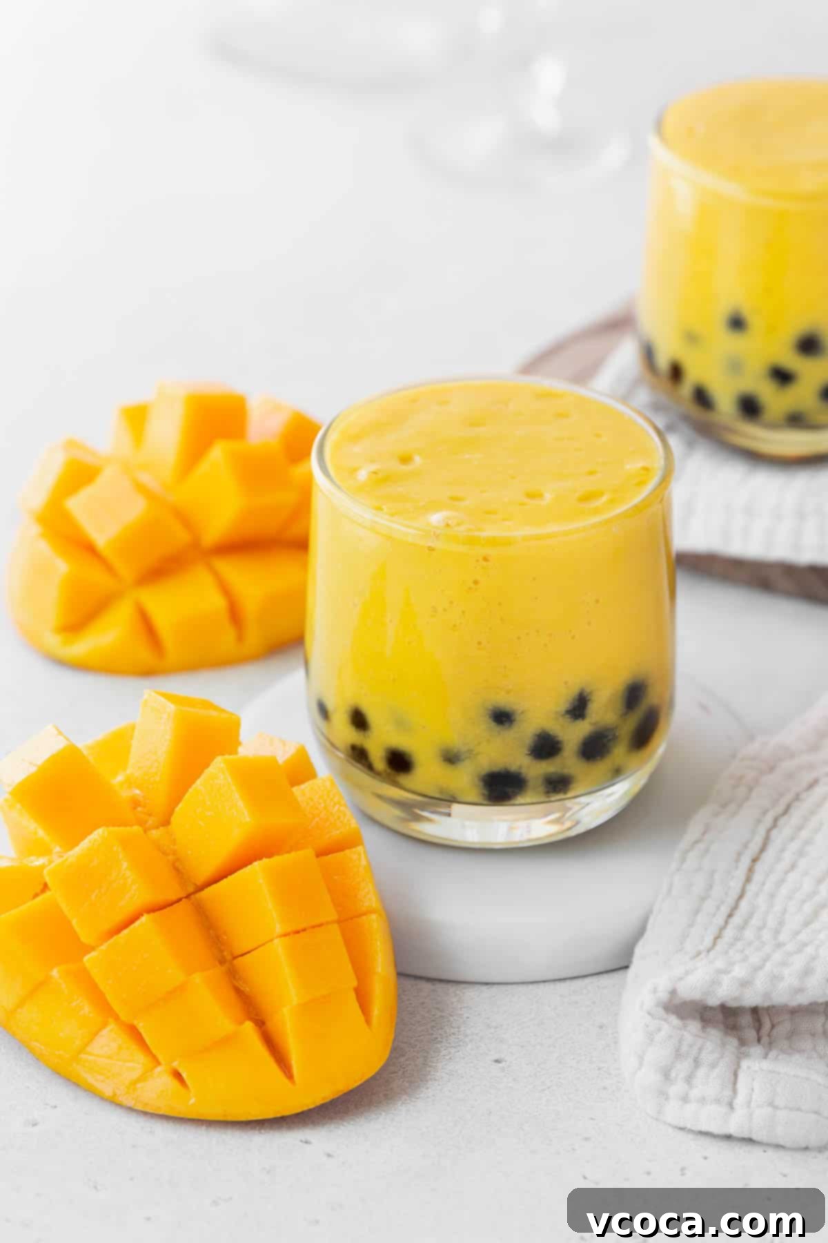 Tropical Mango Boba 4 A closeup shot of a small glass of mango boba tea on a white coaster on the counter next to a sliced up mango.