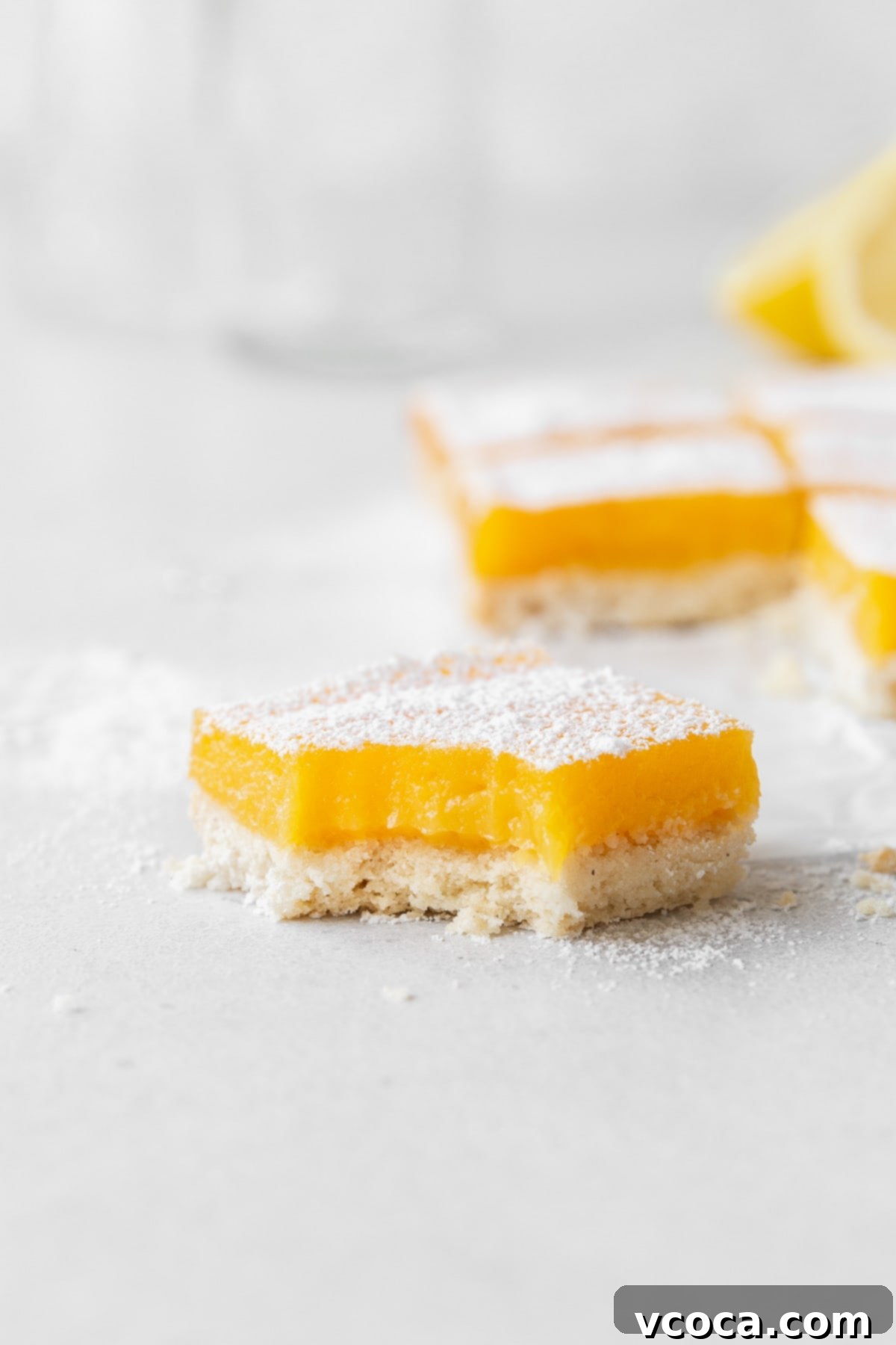 Bright and Zesty Dairy Free Lemon Bars 22 A side shot of a single dairy-free lemon bar with a bite taken out of it, showcasing the filling and crust.
