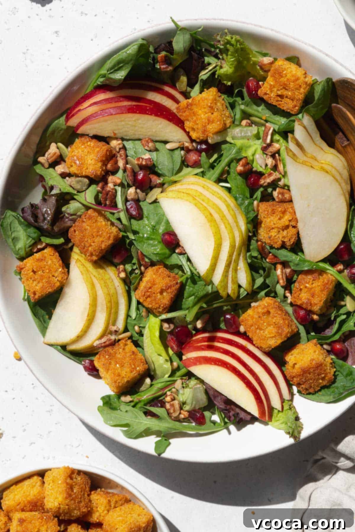 A large bowl of salad with sliced apples, pears, and cornbread croutons.