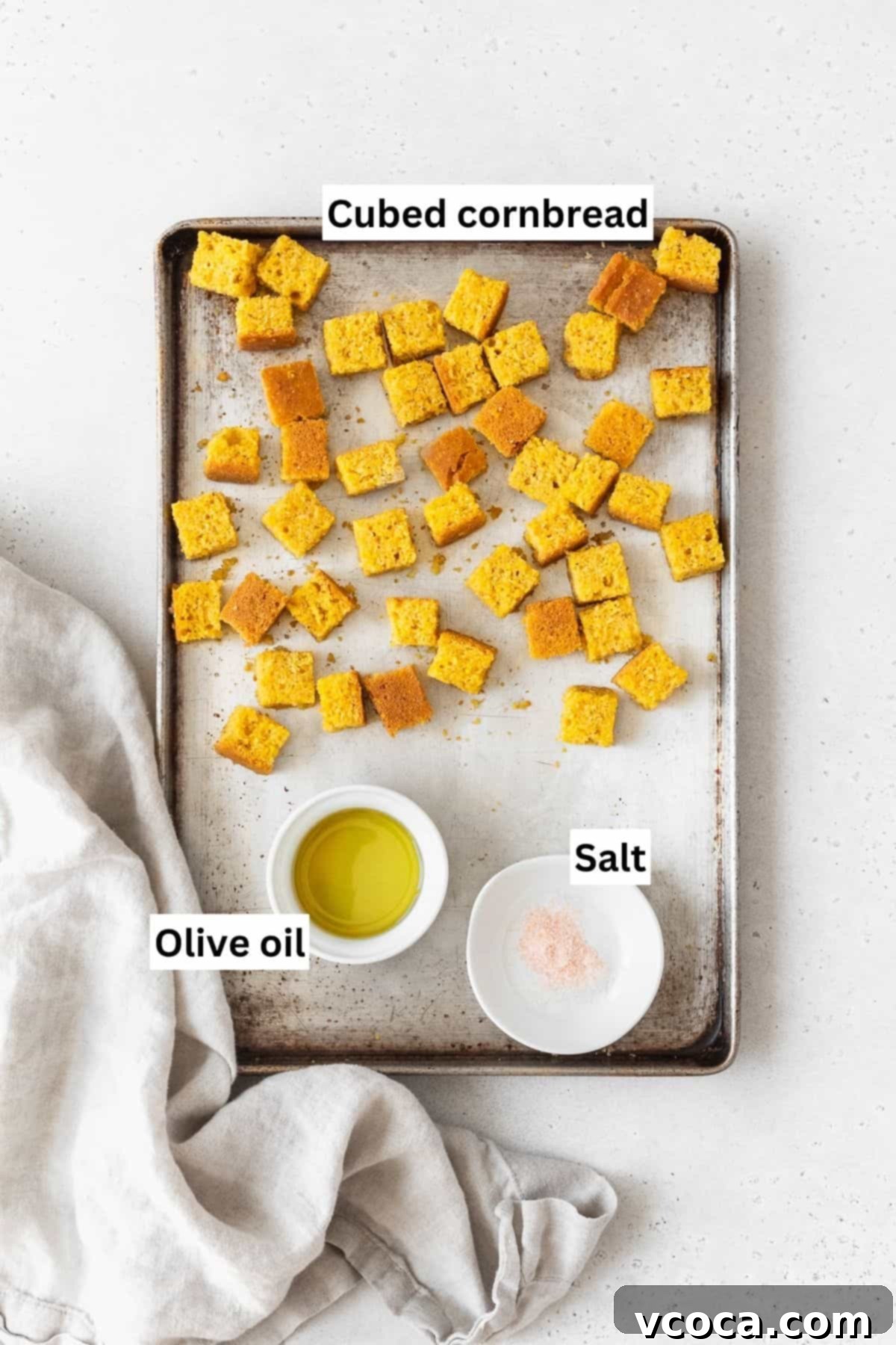 A baking sheet with cubed cornbread, olive oil, and salt.