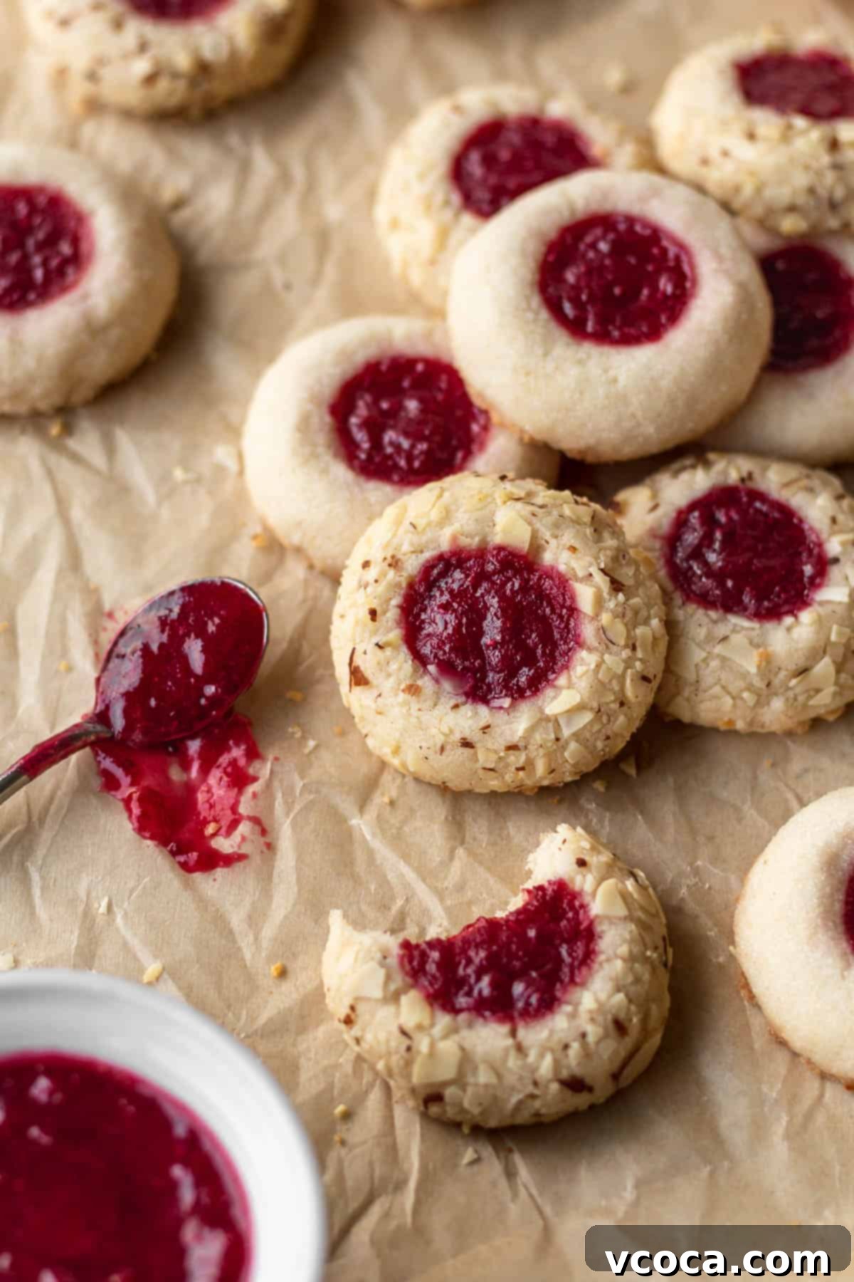 27 Reader-Favorite Gluten-Free Dairy-Free Treats 9 Gluten free thumbprint cookies next to a small spoon of jam on a brown parchment paper.