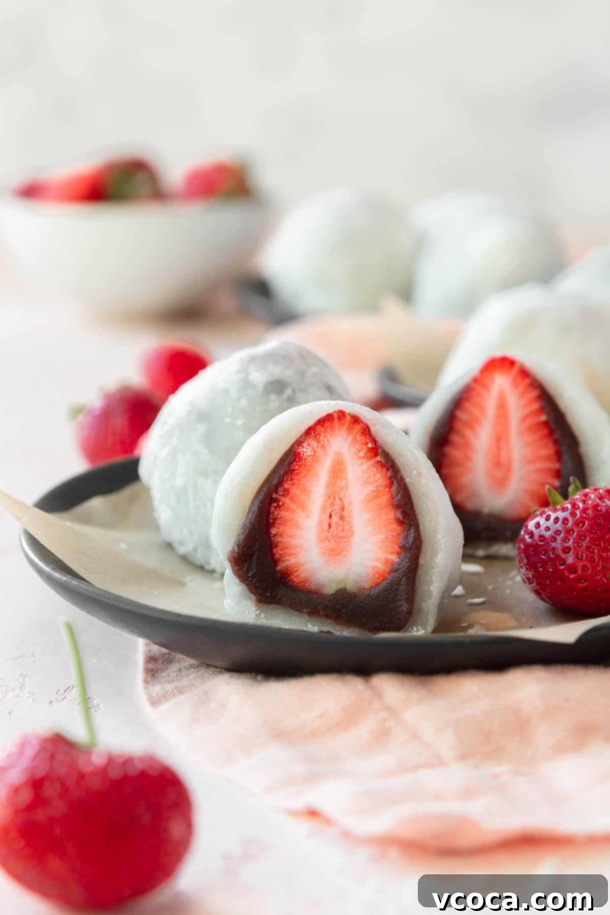 A beautifully sliced Ichigo Daifuku placed on a sleek black plate, revealing its vibrant strawberry and creamy filling. A piece of parchment paper adds a delicate touch to the presentation.
