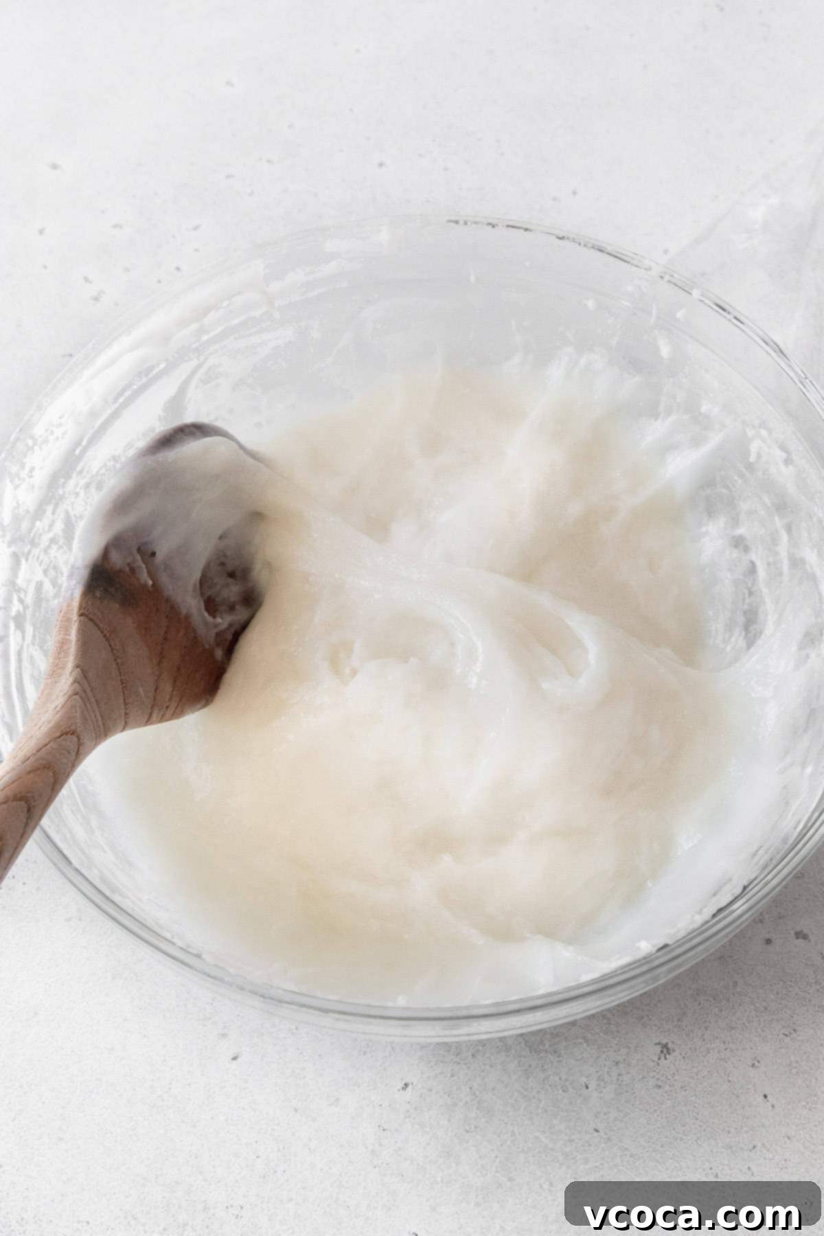 The translucent daifuku mochi dough being thoroughly mixed with a sturdy wooden spoon in a glass bowl, ensuring a uniform and elastic texture.