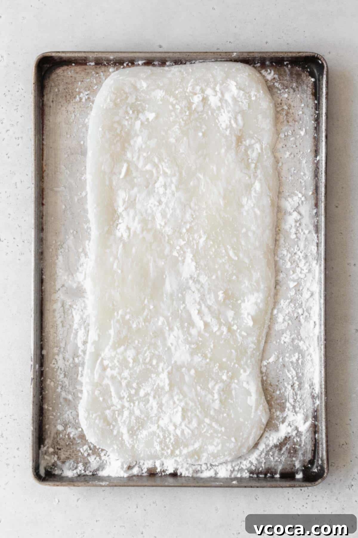 The flattened mochi dough, spread into a smooth rectangle on a baking sheet generously dusted with potato starch, ready for precise cutting.
