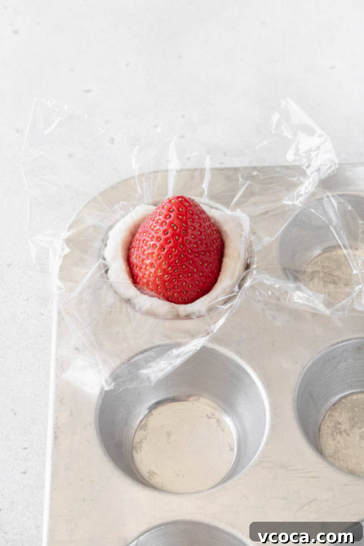 A vibrant red strawberry carefully nestled into a portion of whipped cream within a mini muffin tin, with its tip pointing elegantly upwards.