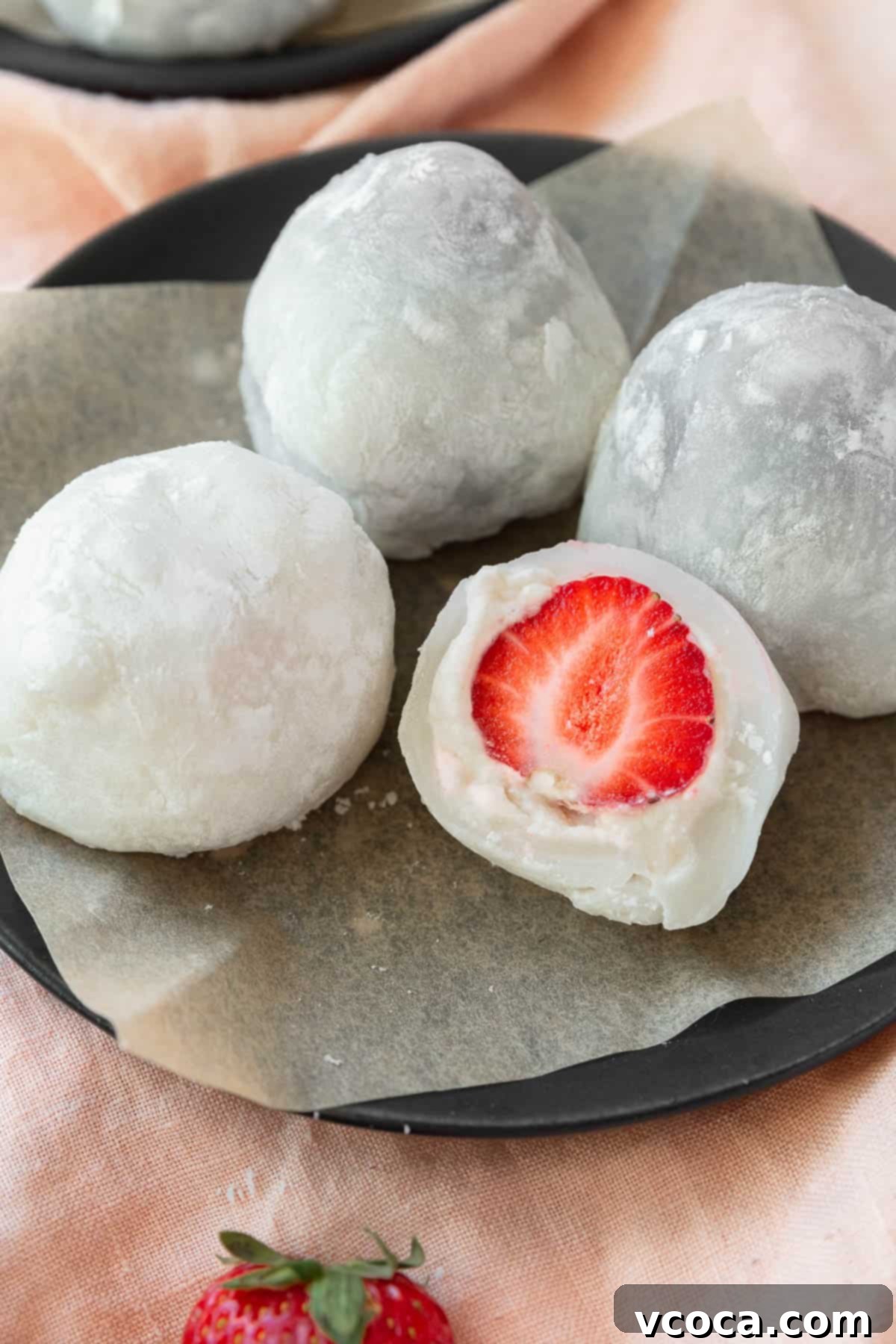 A charming plate displays an array of freshly made strawberry mochi, with one thoughtfully sliced in half to showcase its luscious strawberry and creamy white filling.