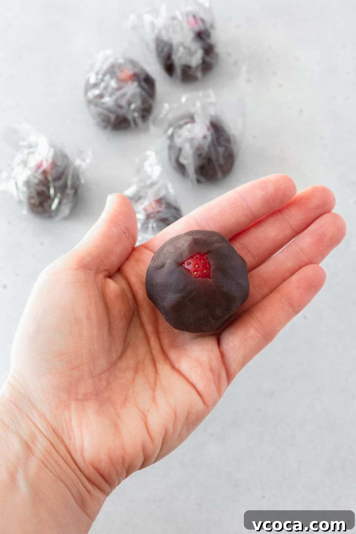 A perfectly wrapped strawberry, fully enrobed in smooth anko, rests on the palm of a hand, showcasing the completion of the filling preparation.