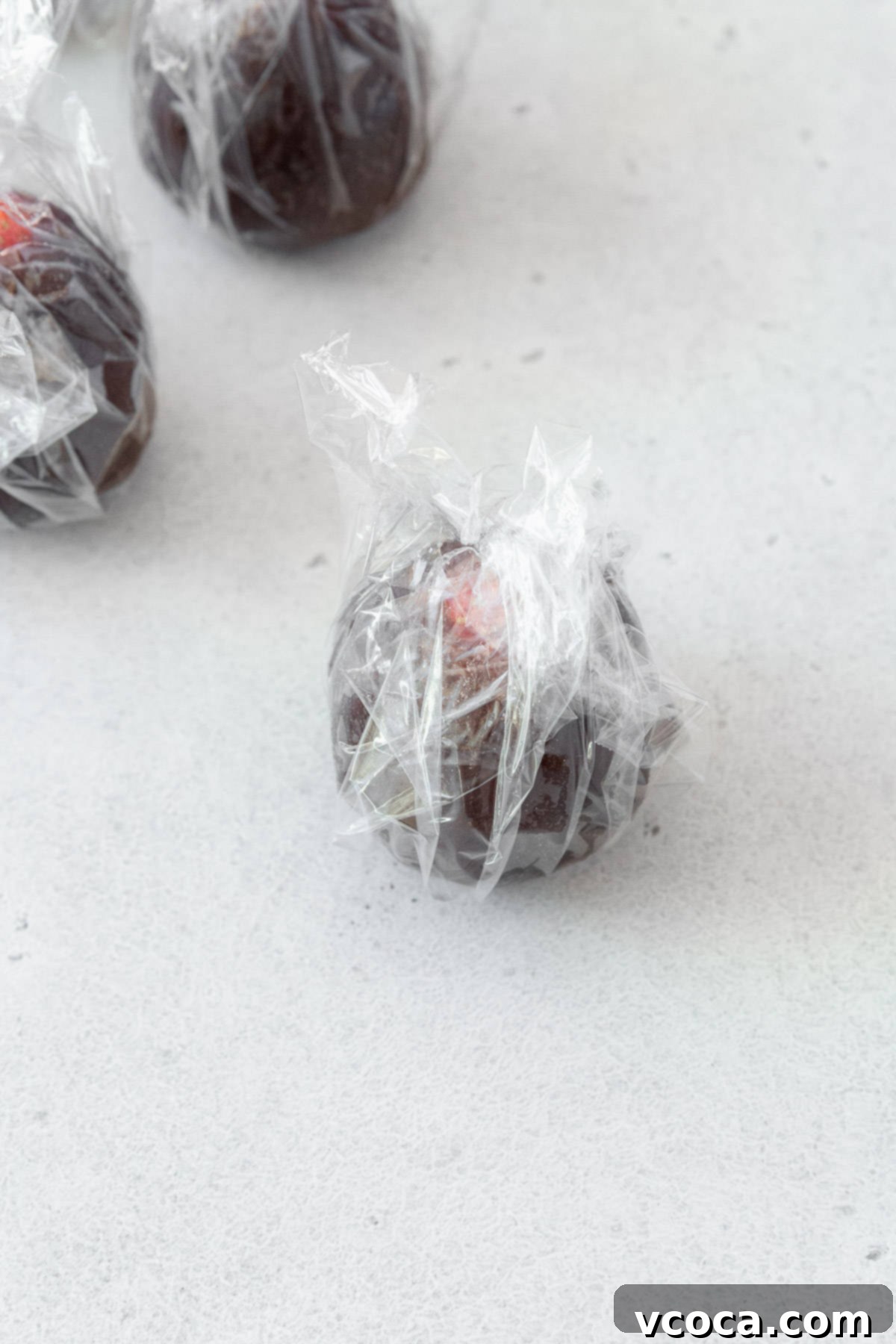 Anko-wrapped strawberry securely encased in plastic wrap, demonstrating a key step to prevent drying before being incorporated into the mochi dough.