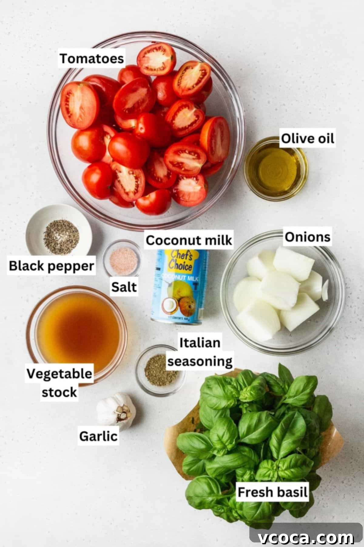 Heartwarming Roasted Tomato Soup 3 Organized bowls showcasing all the fresh ingredients required for making roasted tomato soup, including vibrant red tomatoes, yellow onions, a garlic bulb, fresh basil, and bottles of olive oil and coconut milk.