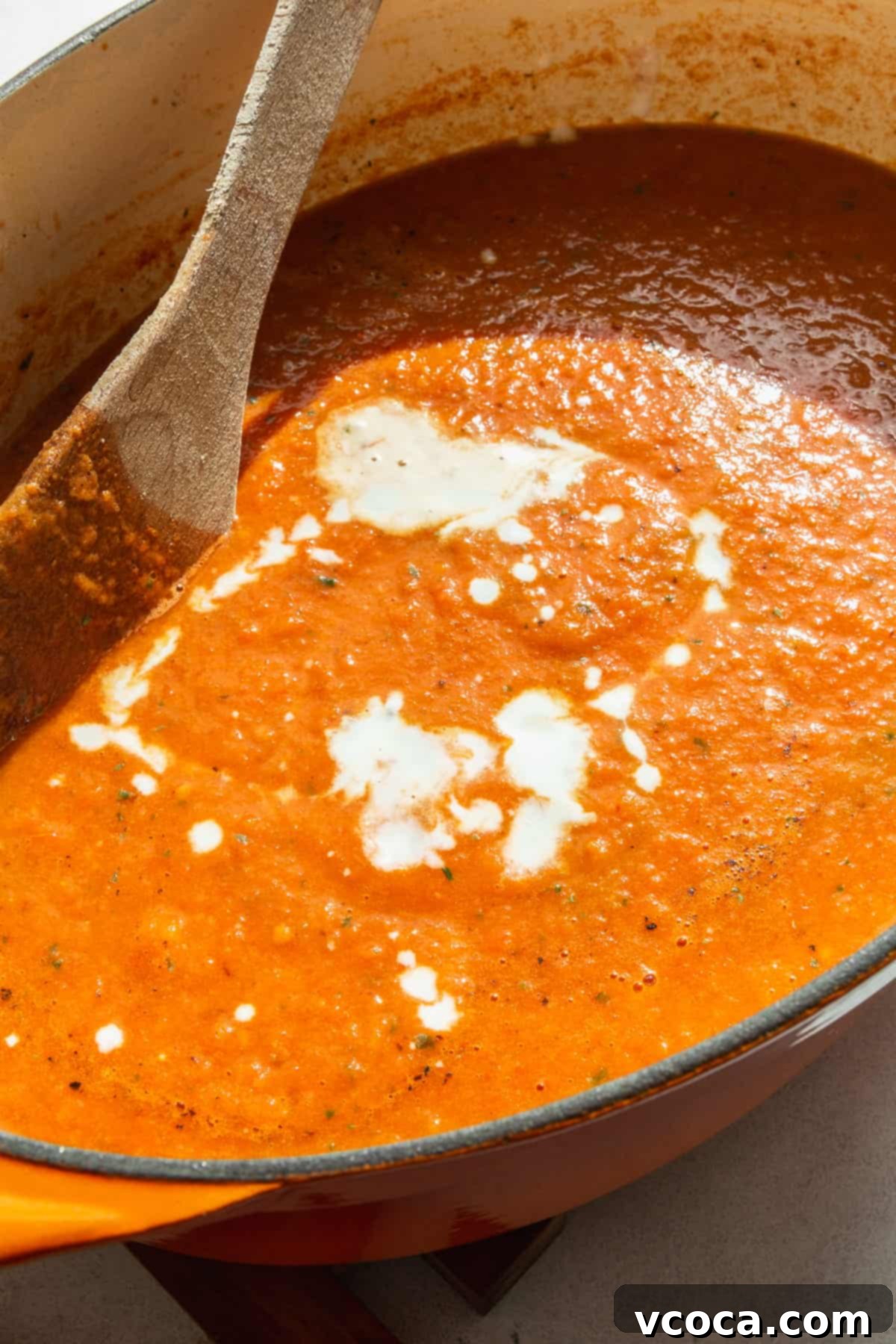 Heartwarming Roasted Tomato Soup 9 A pot of beautifully blended tomato basil soup, with a swirl of rich coconut milk being incorporated, highlighting its creamy texture.