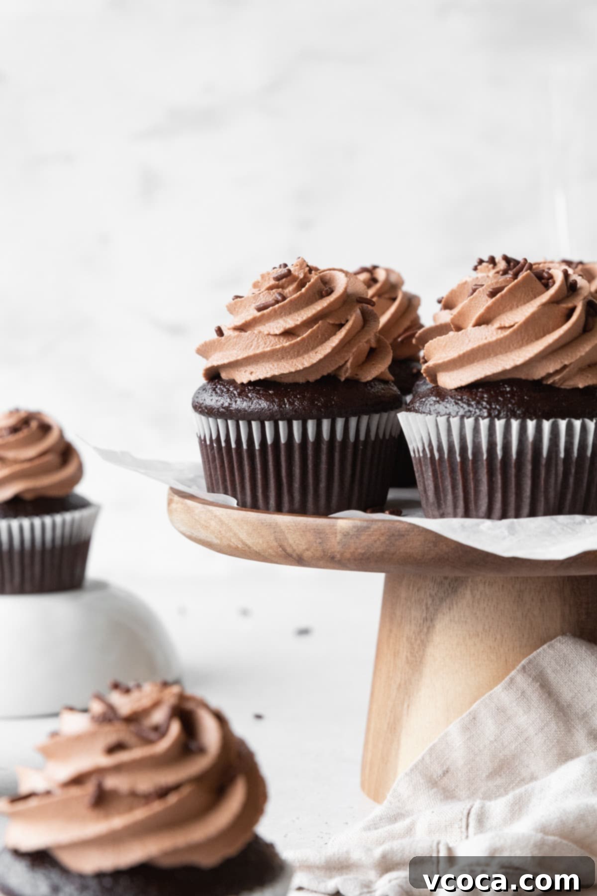 Velvety Chocolate Cupcakes 14 Moist chocolate cupcakes with chocolate frosting on a wooden cake stand.