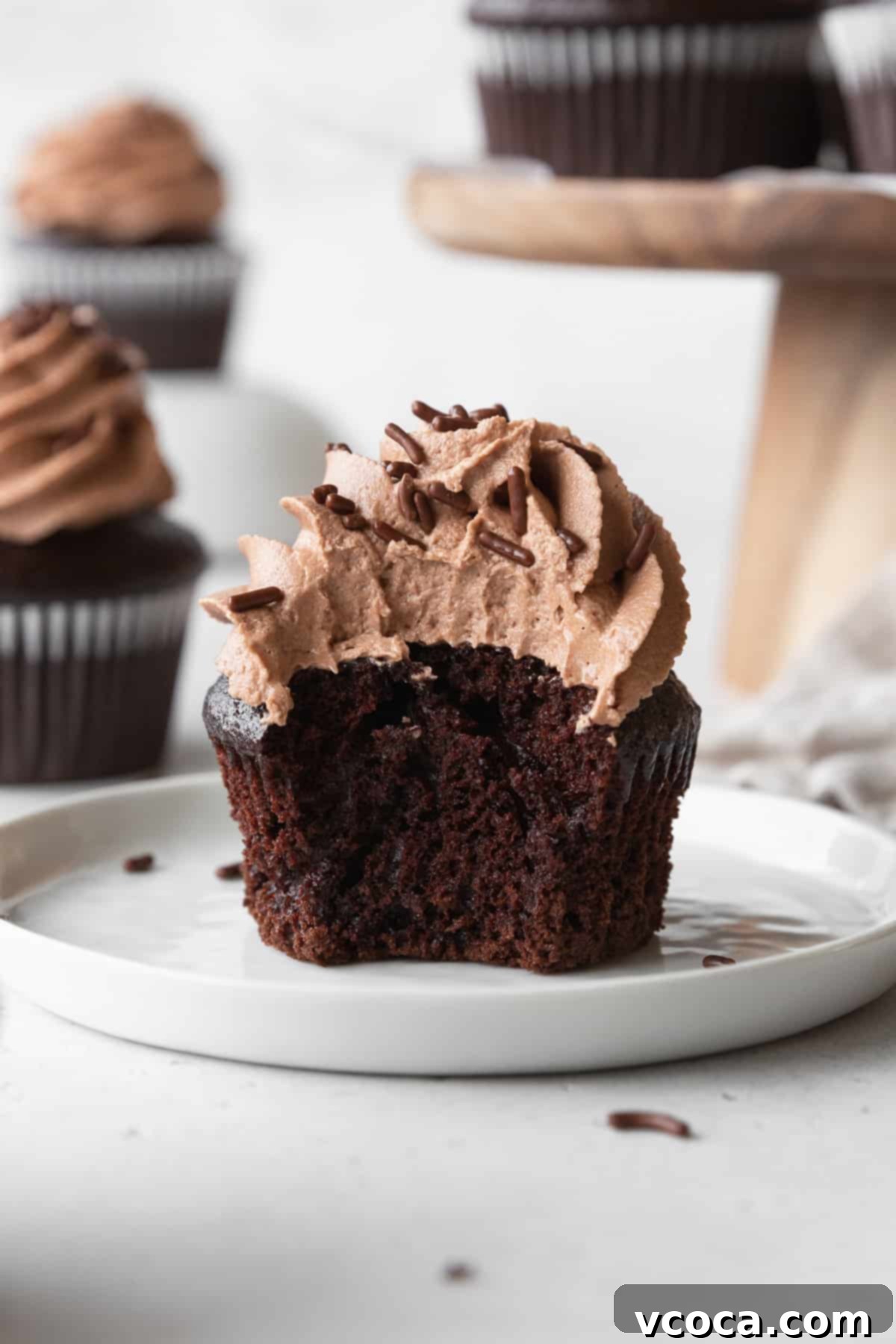 Velvety Chocolate Cupcakes 15 A bitten chocolate cupcake with chocolate frosting on a white plate.