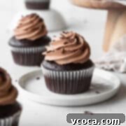 Velvety Chocolate Cupcakes 17 A chocolate cupcake with chocolate frosting on a white dessert plate.