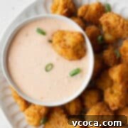 A deep fried cauliflower being dipped into a bowl of bang bang sauce, highlighting the creamy texture.