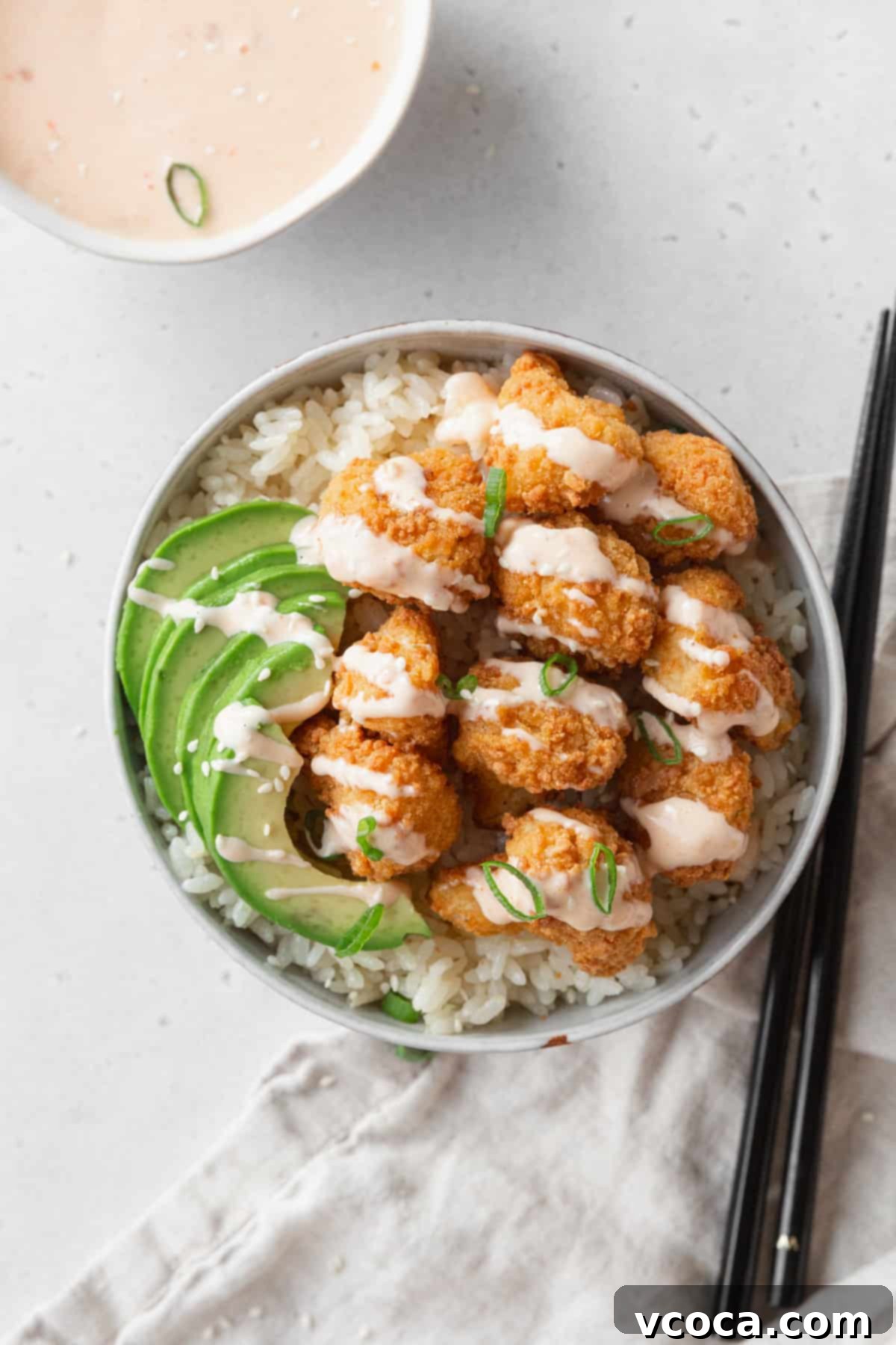 A vibrant bowl of coconut rice topped with crispy Bang Bang cauliflower, fresh avocado slices, and a generous drizzle of the homemade sauce.